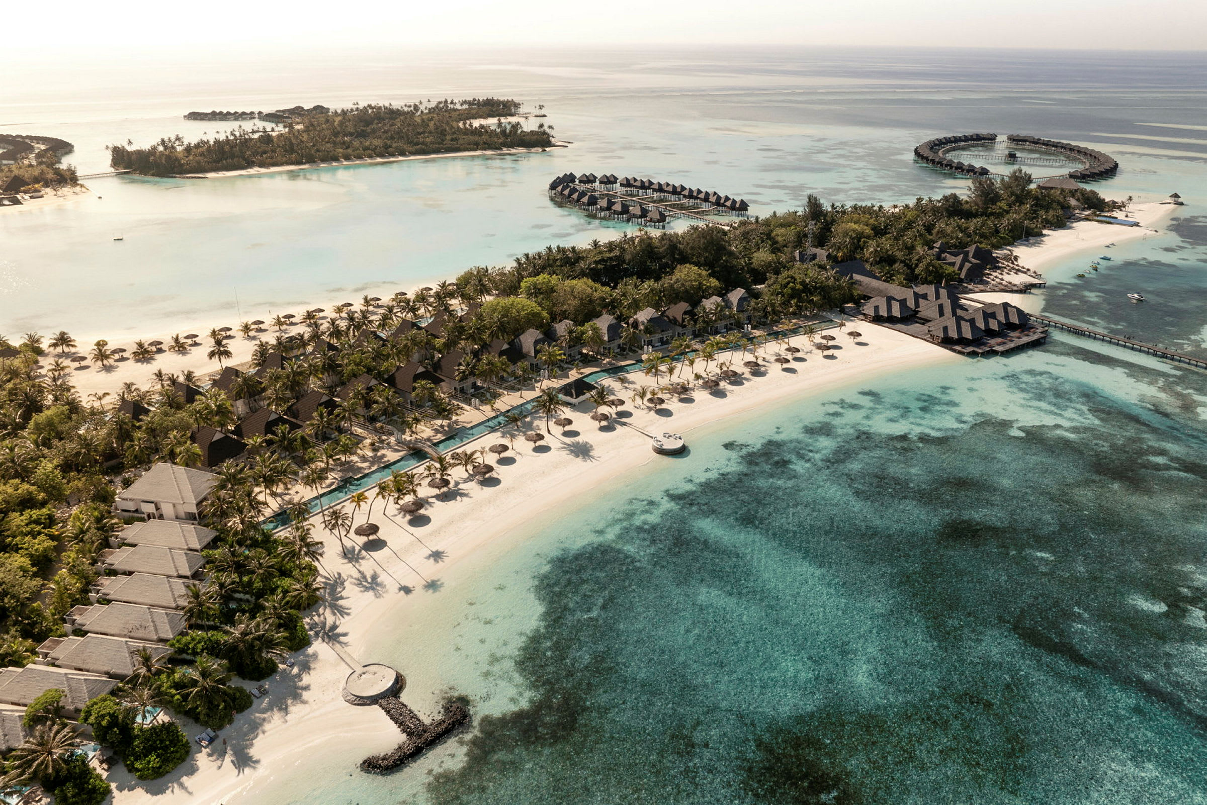 Flygbild av en tropisk resort vid stranden med bungalows, pooler och omgivande klarblått hav. (AI-genererad text)