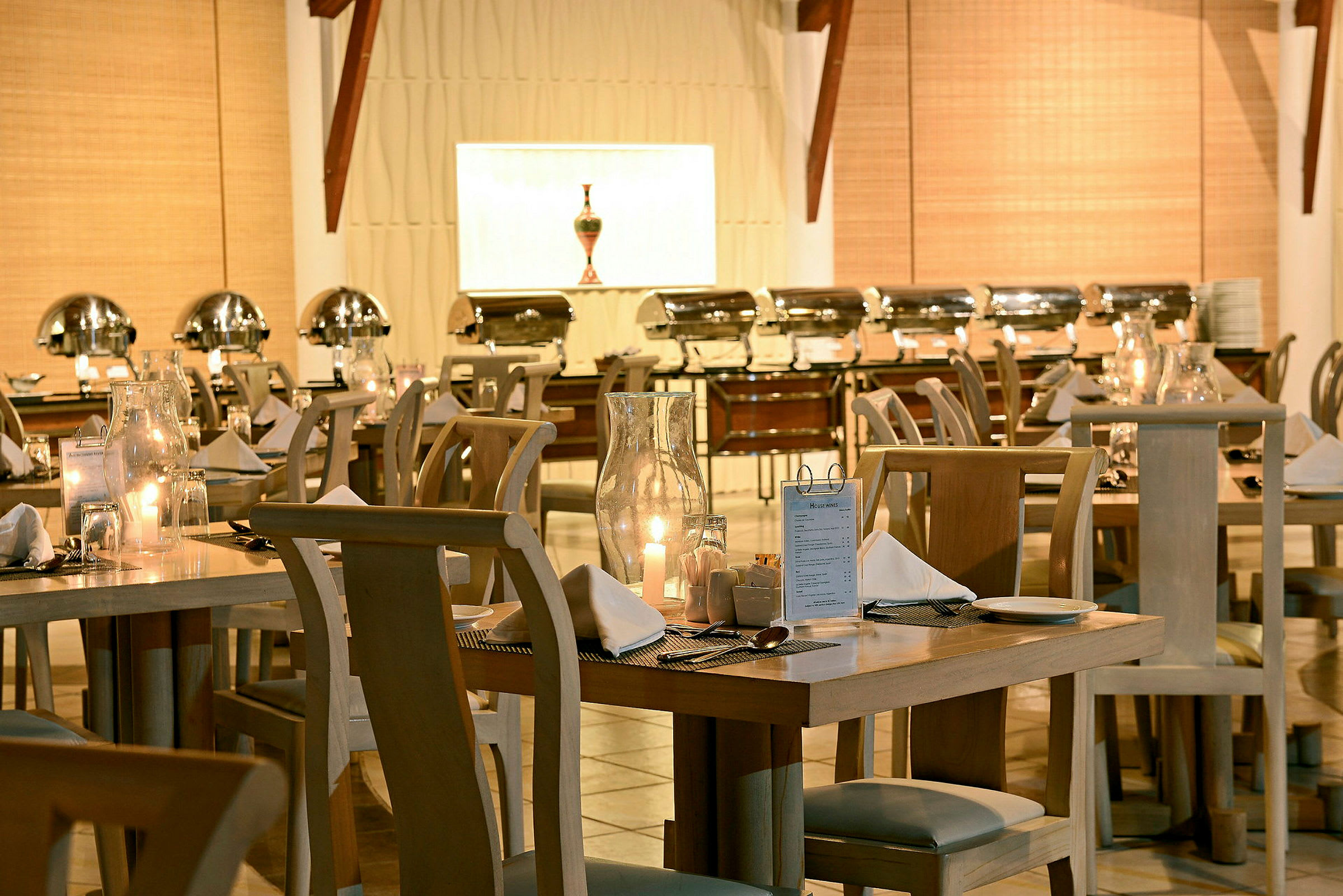 Bild föreställande en upplyst restaurang med dukade bord och bufféstationer i bakgrunden. (AI-genererad text)