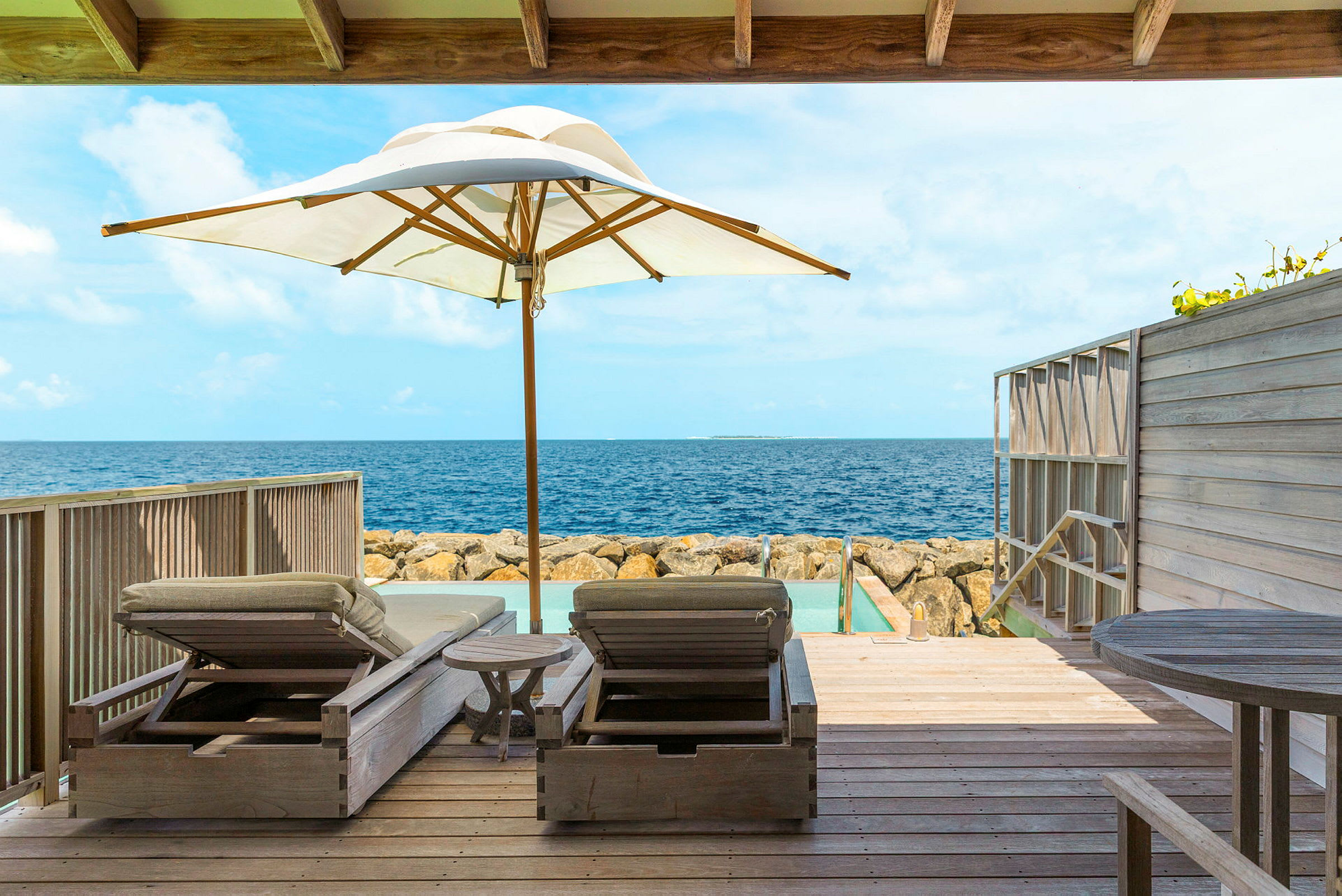 Två solstolar och ett parasoll på en träveranda med utsikt över havet. (AI-genererad text)