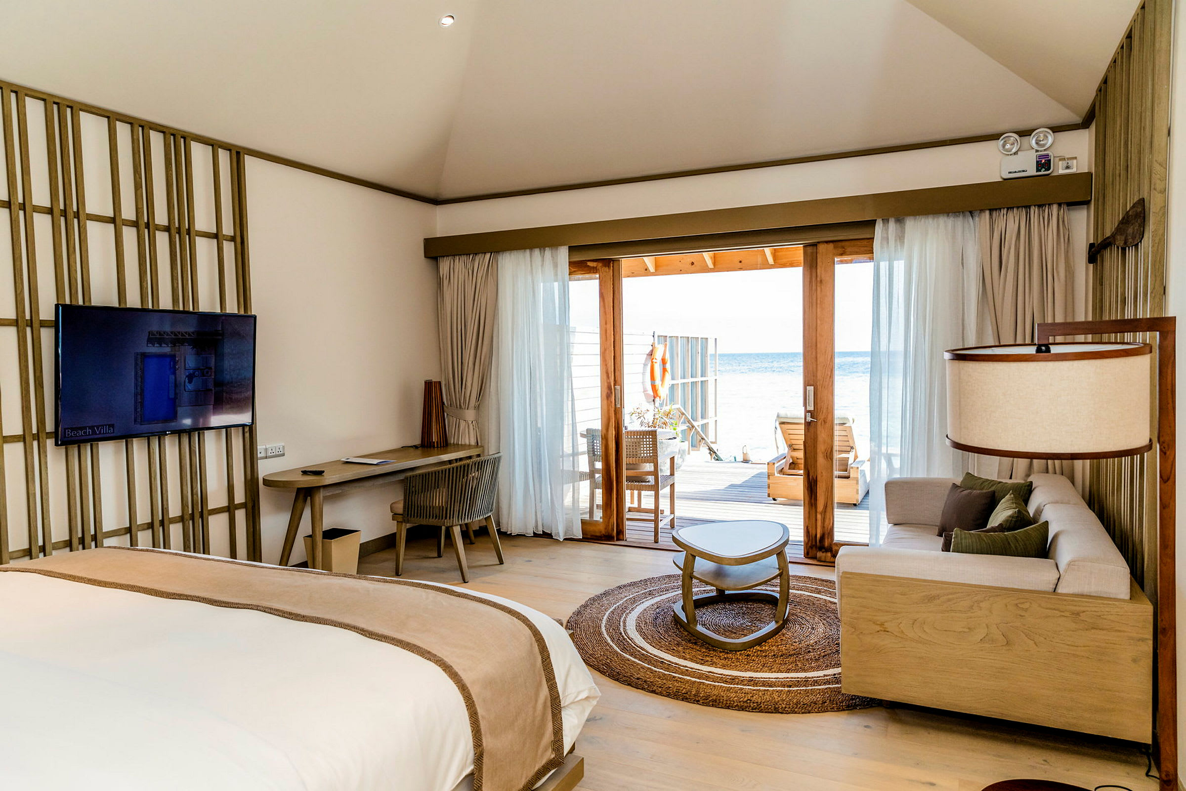 Interiör av en strandvilla med moderna möbler, en sittgrupp och säng, samt en terrass med utsikt över havet. (AI-genererad text)