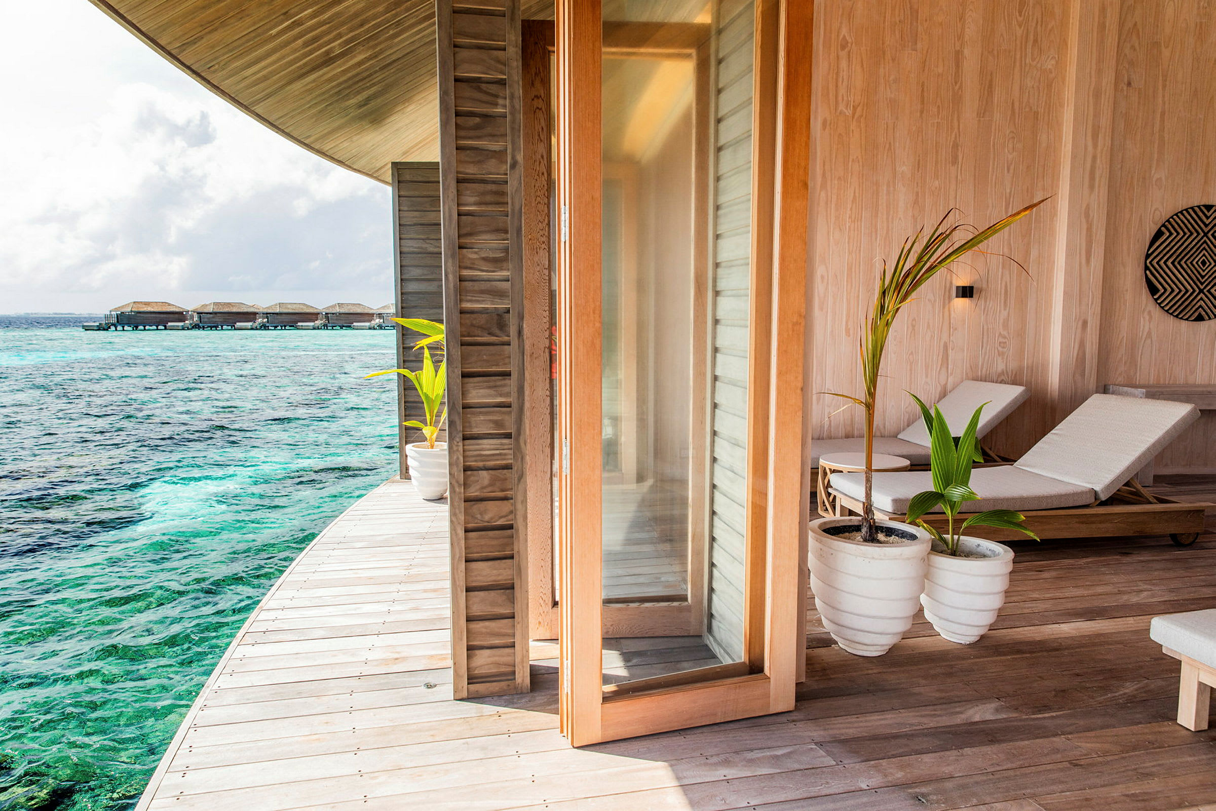 Bild av en veranda med solstolar och en utsikt över turkost hav och bungalower över vattnet. (AI-genererad text)