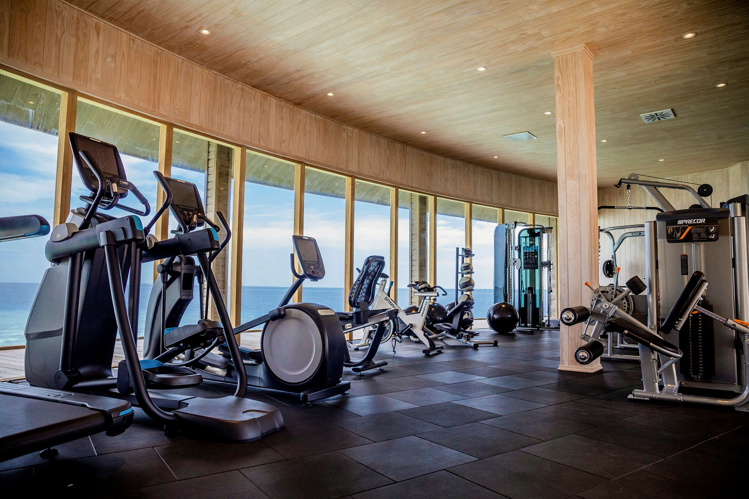 Ett gym med träningsmaskiner och stora fönster som vetter mot havet. (AI-genererad text)
