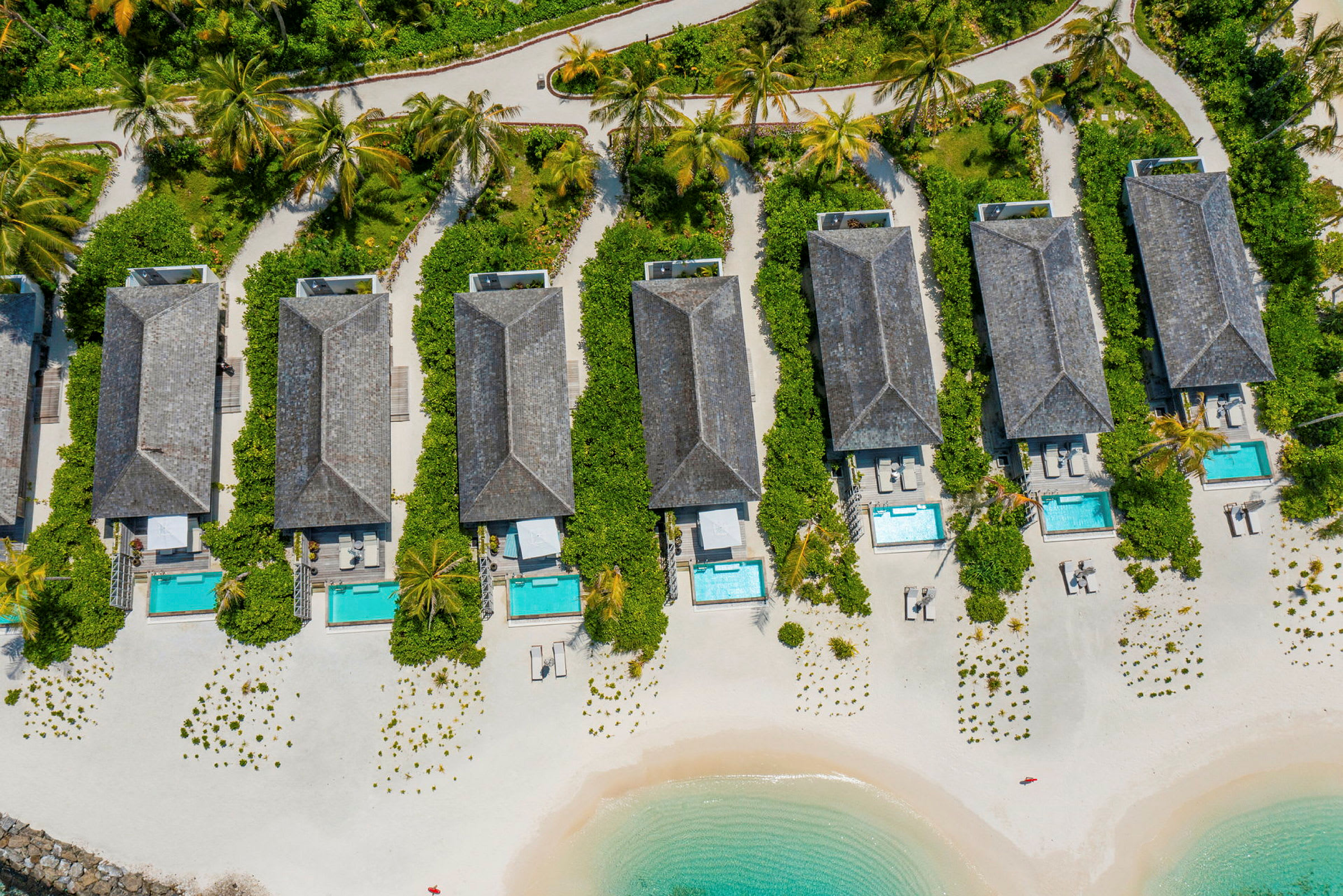 Flygvy av strandvillor med privat pooler och trädgårdar på en sandstrand vid havet. (AI-genererad text)