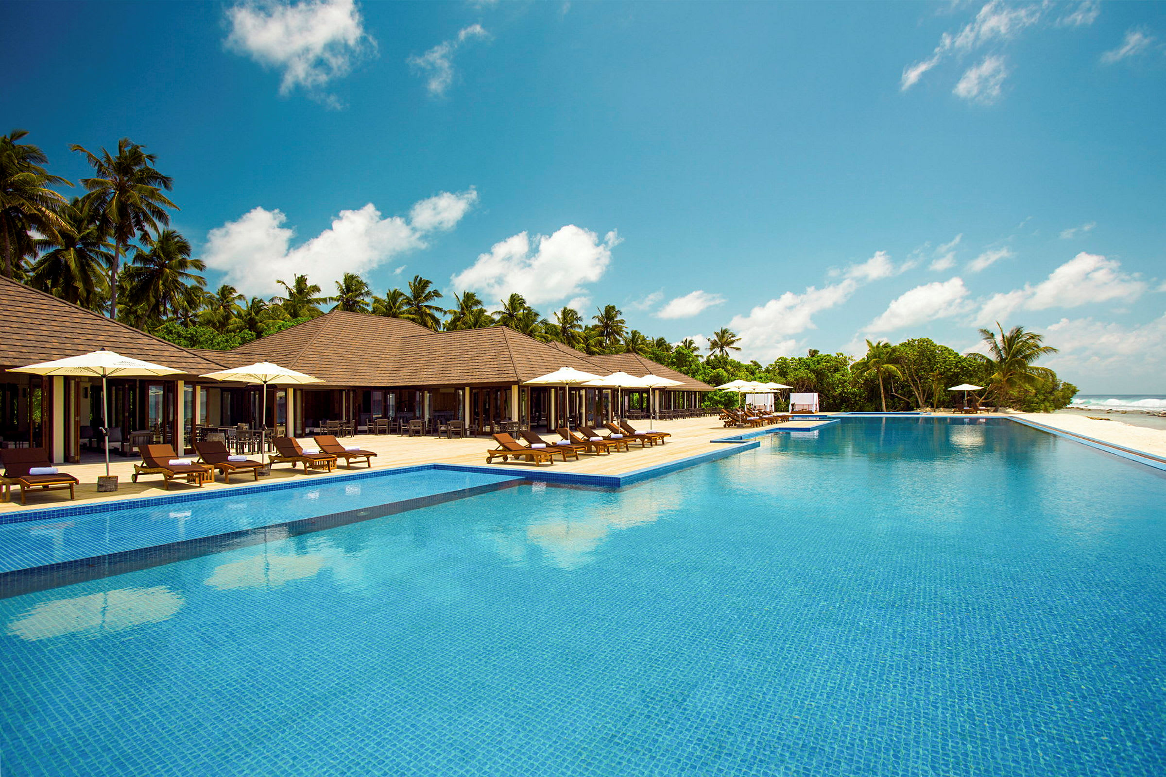 Bild föreställande en infinitypool vid en tropisk resort med solstolar, parasoll och palmer. (AI-genererad text)