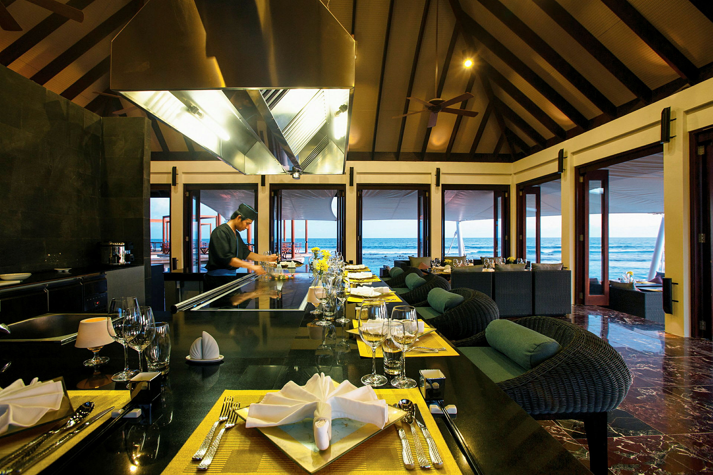Restaurang vid havet med dukade bord och öppna dörrar mot utsikten. (AI-genererad text)