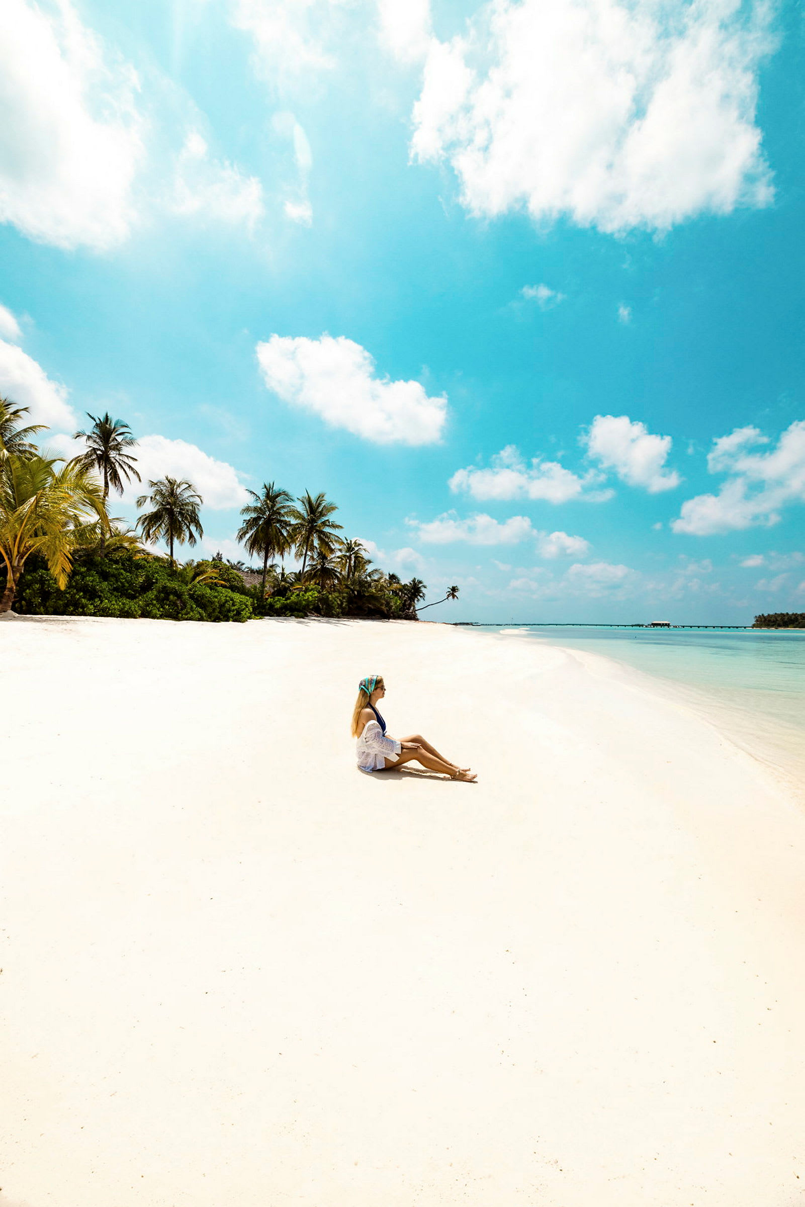 En person sitter på en vit sandstrand med palmer och en klarblå himmel i bakgrunden. (AI-genererad text)