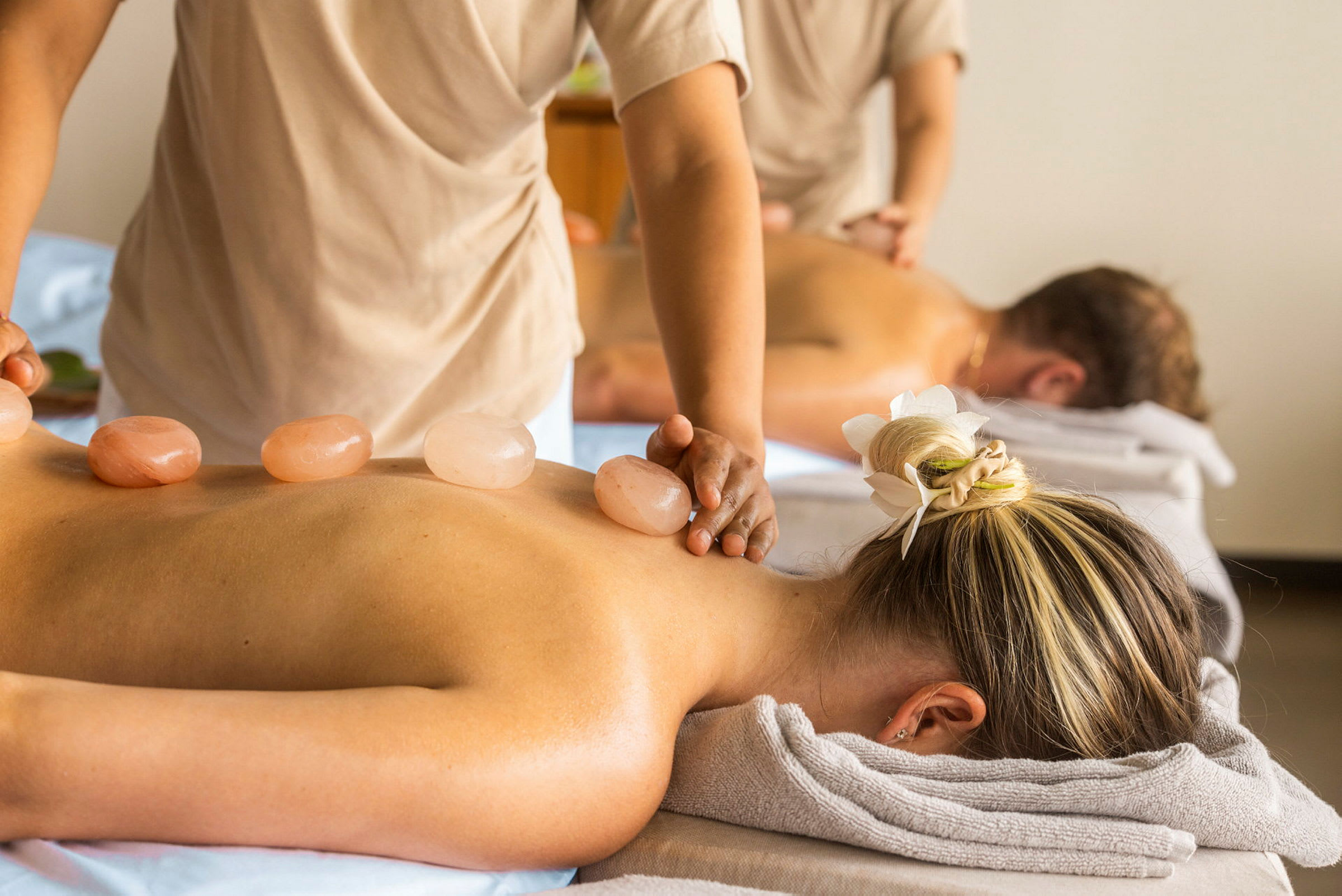 Personer njuter av en massagebehandling på en spa-anläggning. Det finns varma stenar placerade på kroppen. (AI-genererad text)