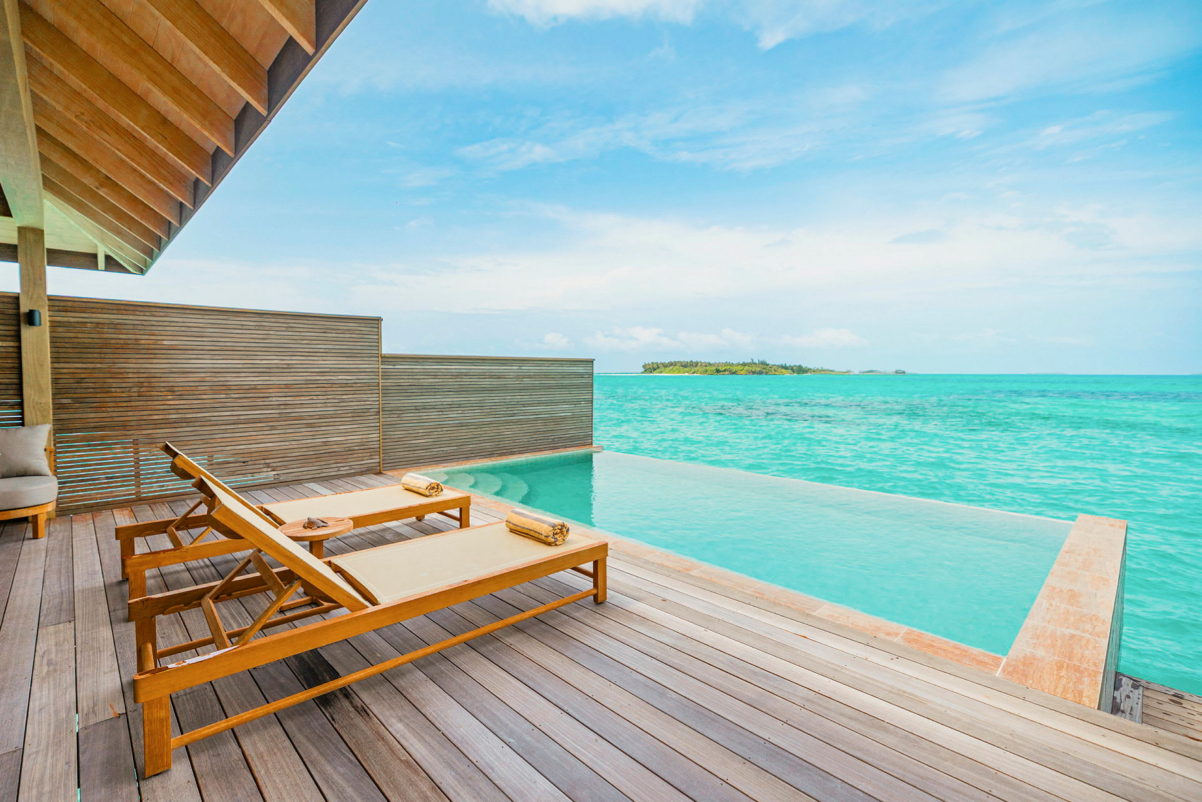 Terrass med två solstolar vid en infinitypool och utsikt över turkost hav. (AI-genererad text)