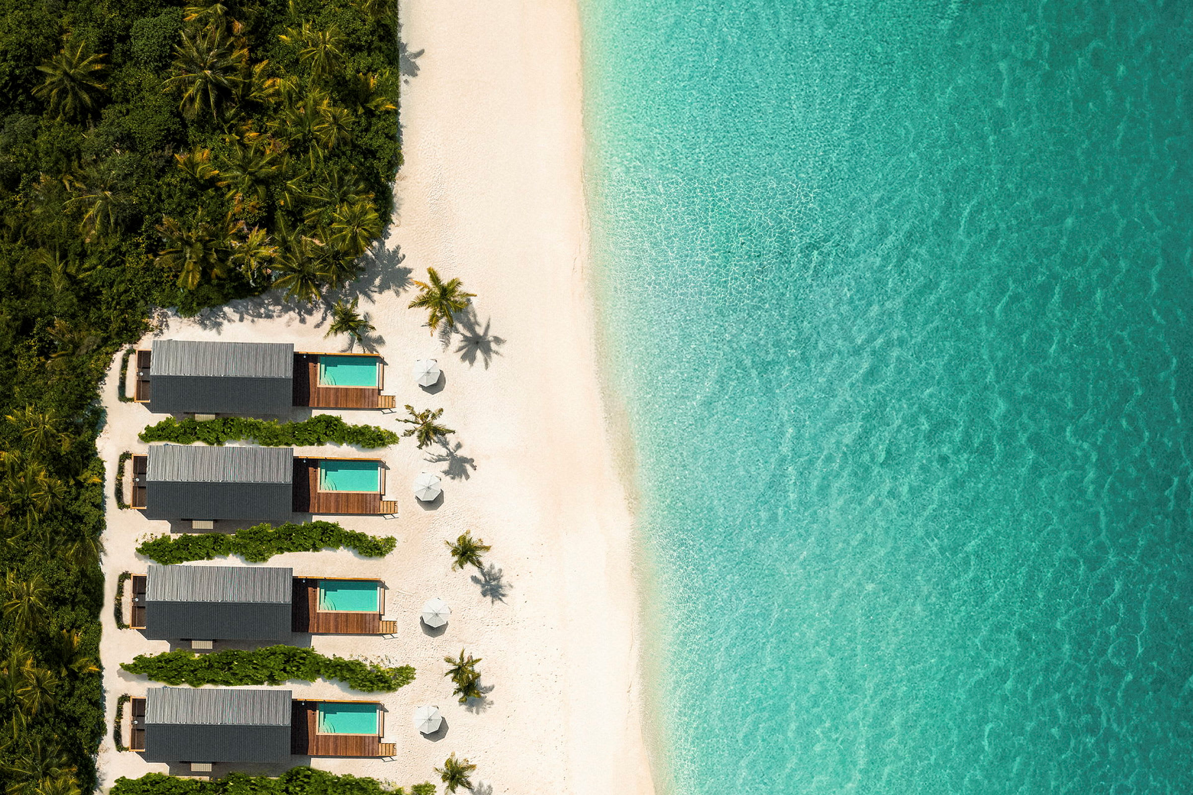 Flygbild av tropiska bungalows med egna pooler längs en sandstrand och med turkost vatten. (AI-genererad text)
