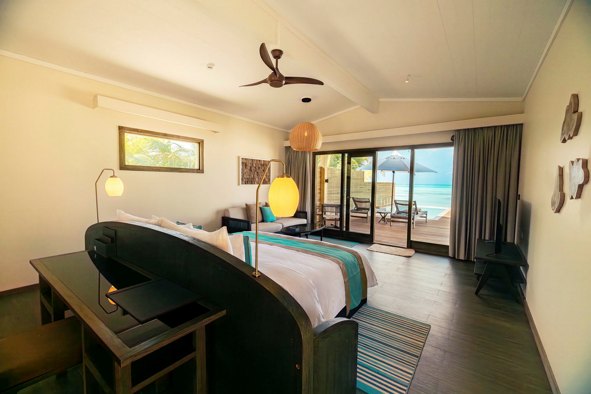 Ett modernt hotellrum med ljus inredning, en säng, soffområde och utgång till en terrass med utsikt över havet. (AI-genererad text)