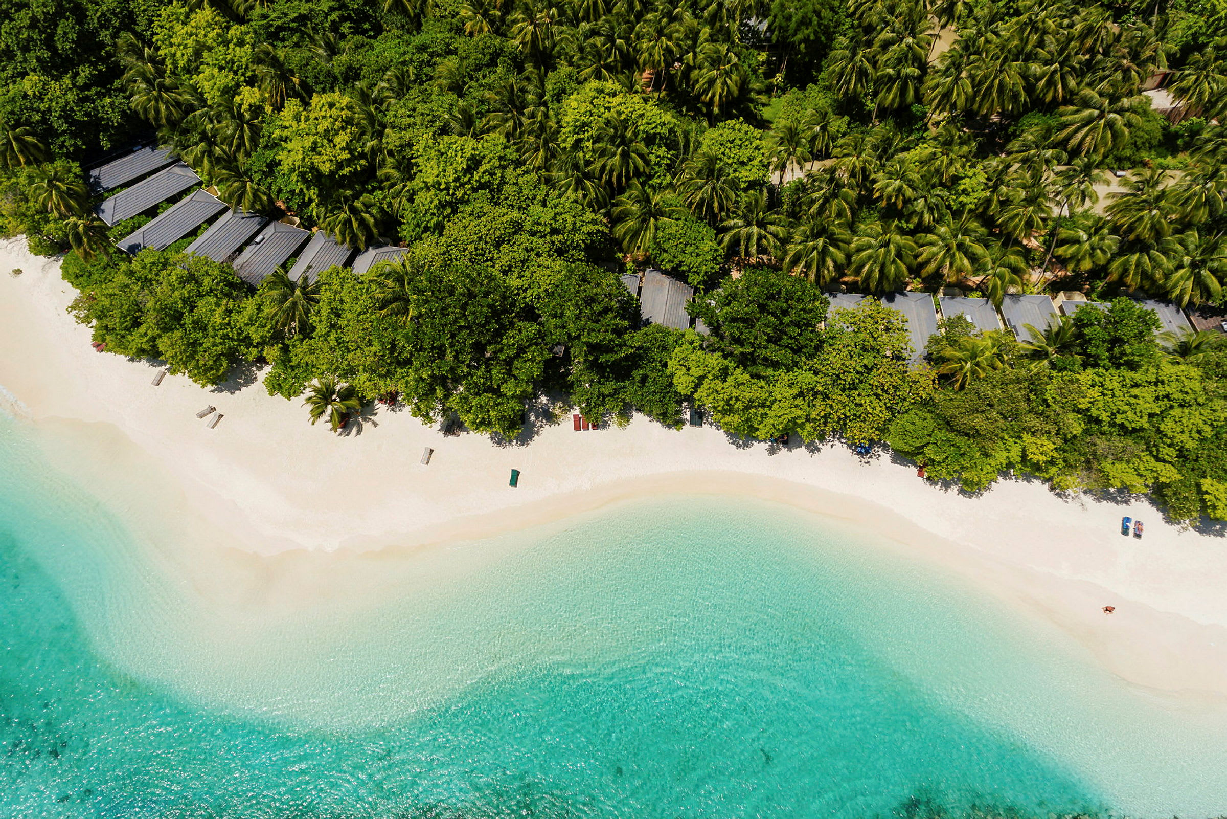Flygfoto som visar en tropisk strand med vit sand, omgiven av klarblått vatten och grönskande vegetation. (AI-genererad text)