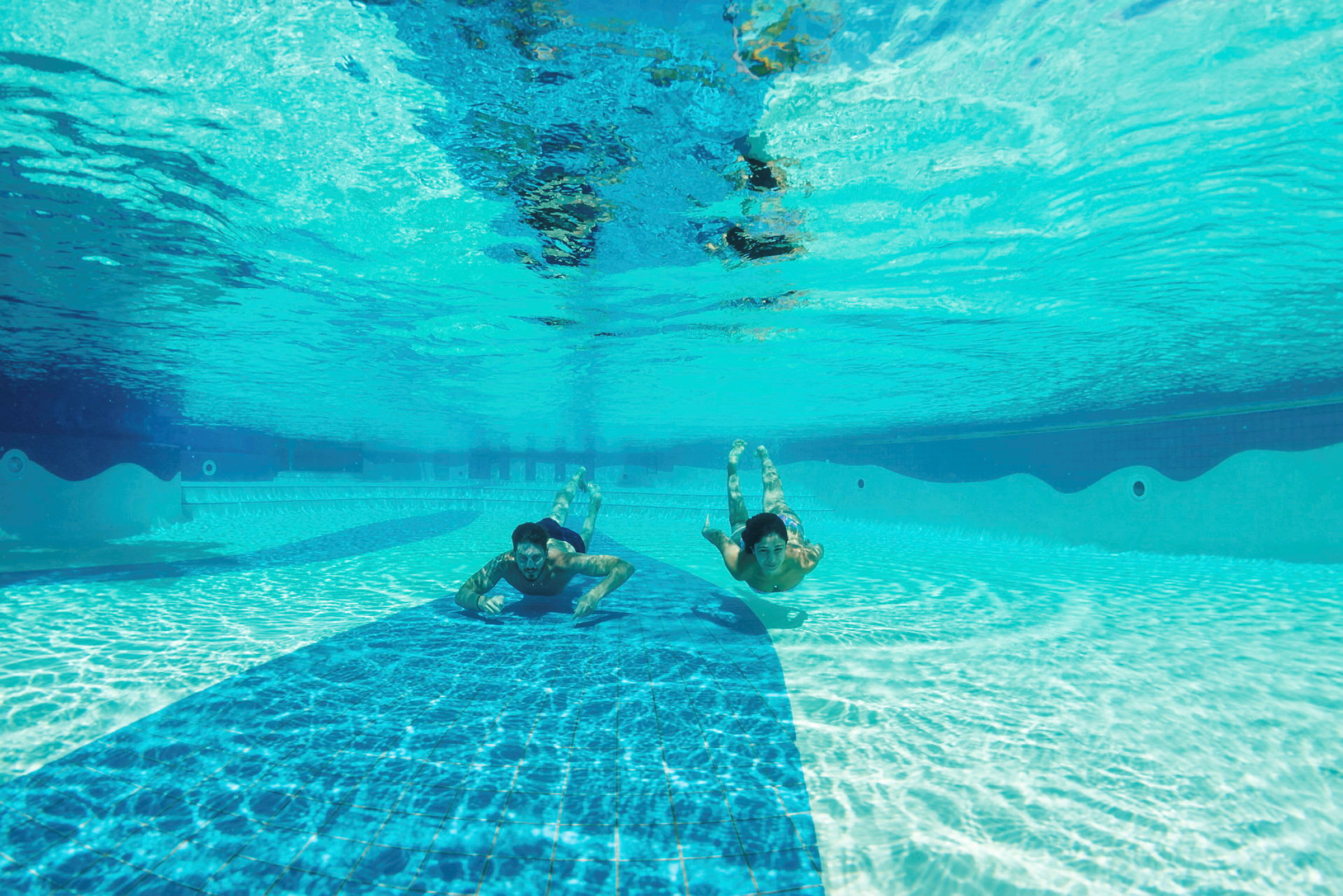 Under vattnet i en klar pool med två personer som simmar. (AI-genererad text)