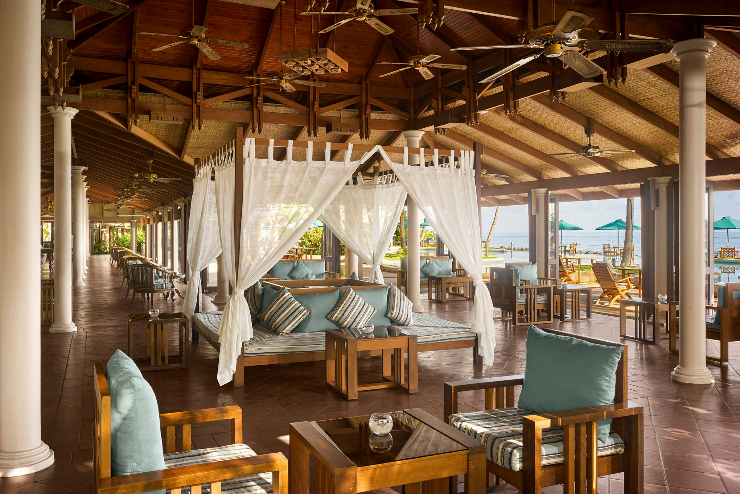 En öppen lounge med träinredning, sittmöbler och dekorerade takfläktar vid havet. (AI-genererad text)