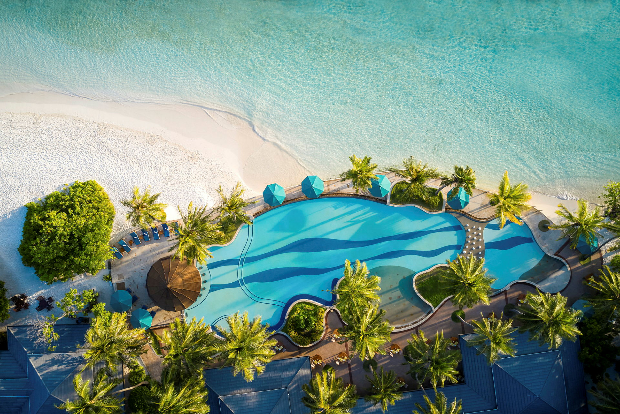 Flygfoto av en pool med palmer bredvid en sandstrand och hav. (AI-genererad text)