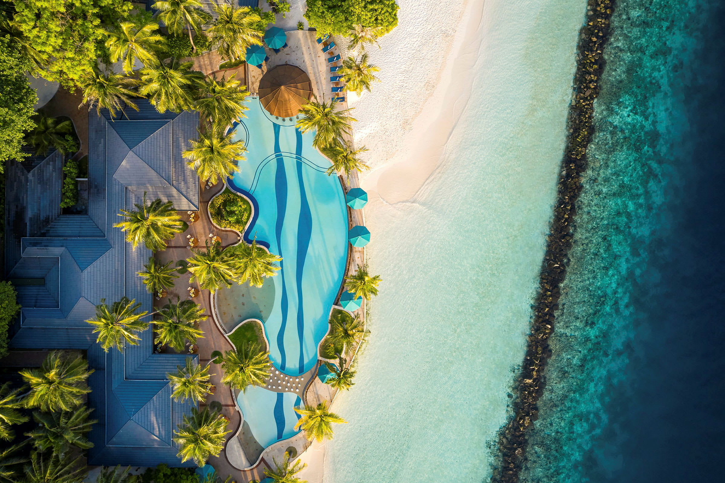 Flygbild av en pool omgiven av träd, strand och hav. (AI-genererad text)