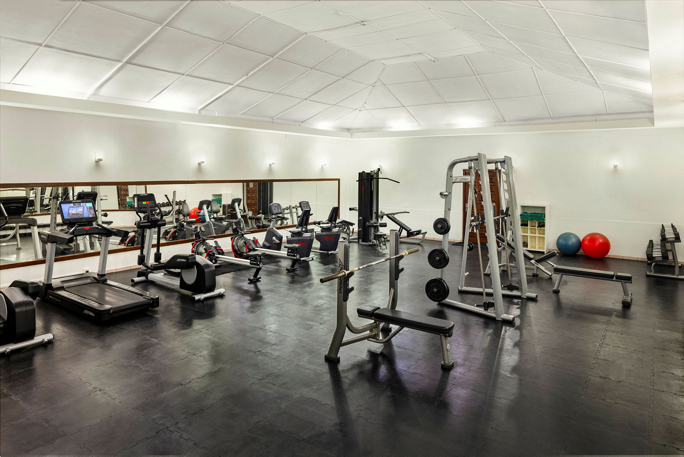 Ett gym med olika träningsmaskiner och utrustning, inklusive löpband, vikter och bänkar. (AI-genererad text)