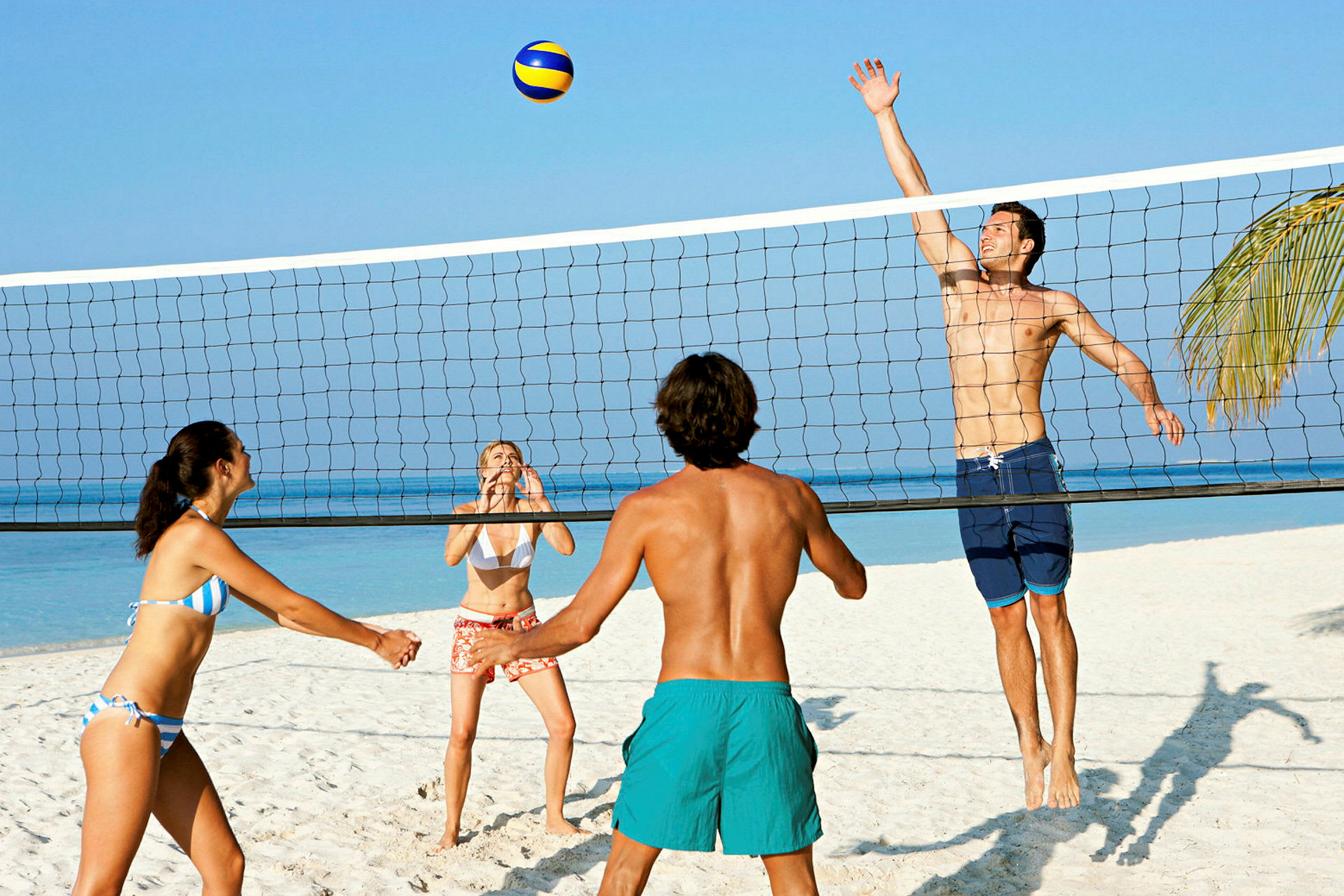 Fyra personer spelar beachvolleyboll på en sandstrand nära havet. (AI-genererad text)
