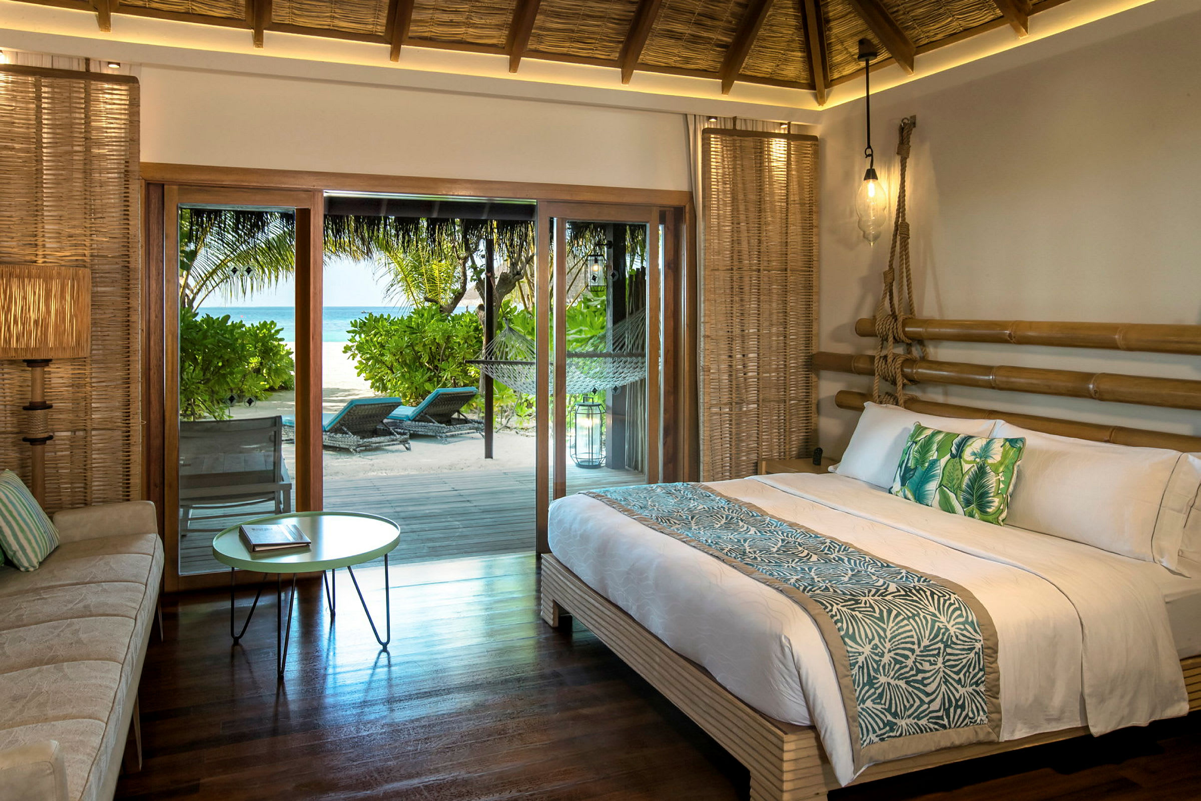 Ett sovrum med en dubbelsäng och tropiska dekorationer, samt en utgång till en terrass med havsutsikt. (AI-genererad text)