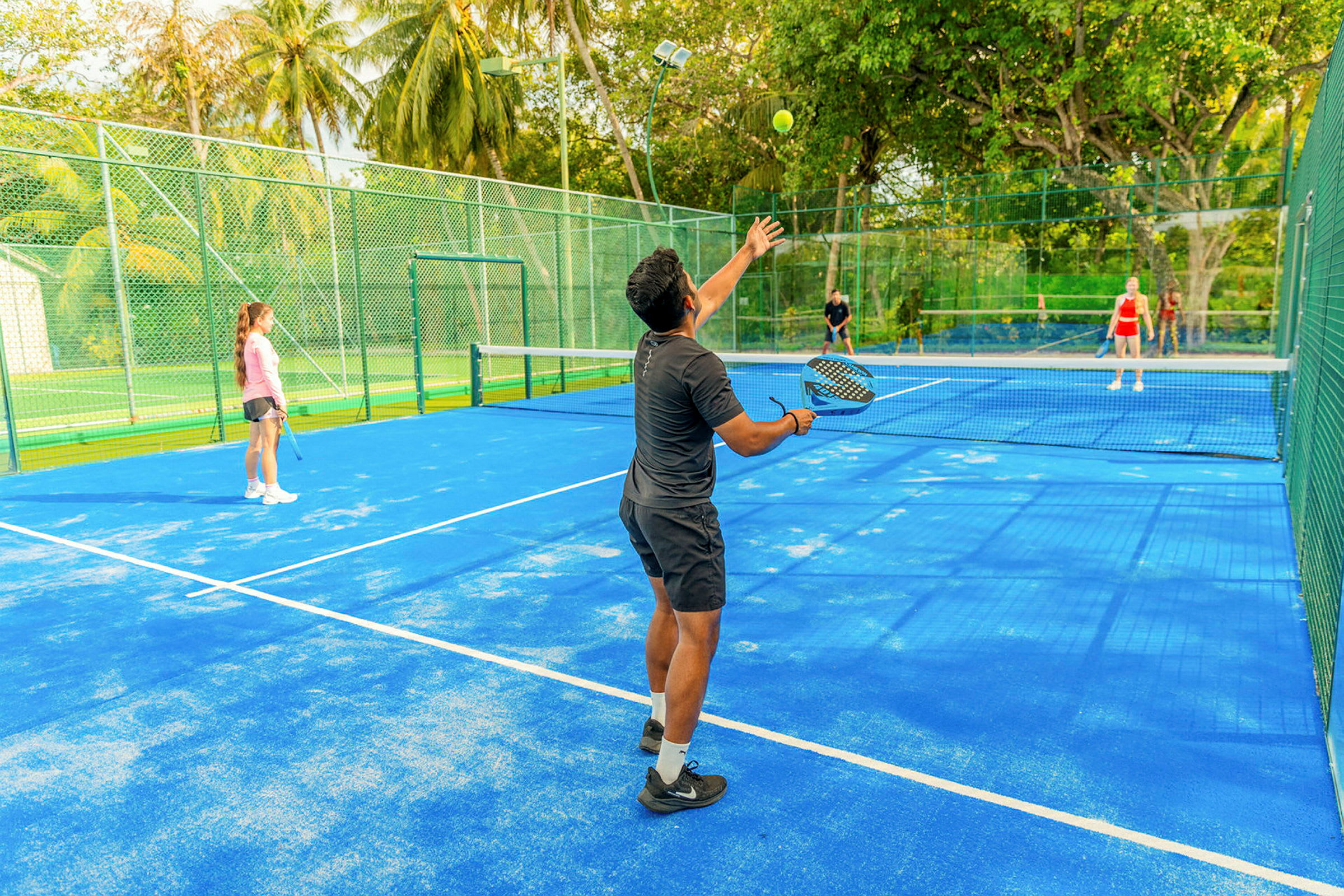 Personer spelar padel på en blå bana omgiven av gröna träd. (AI-genererad text)