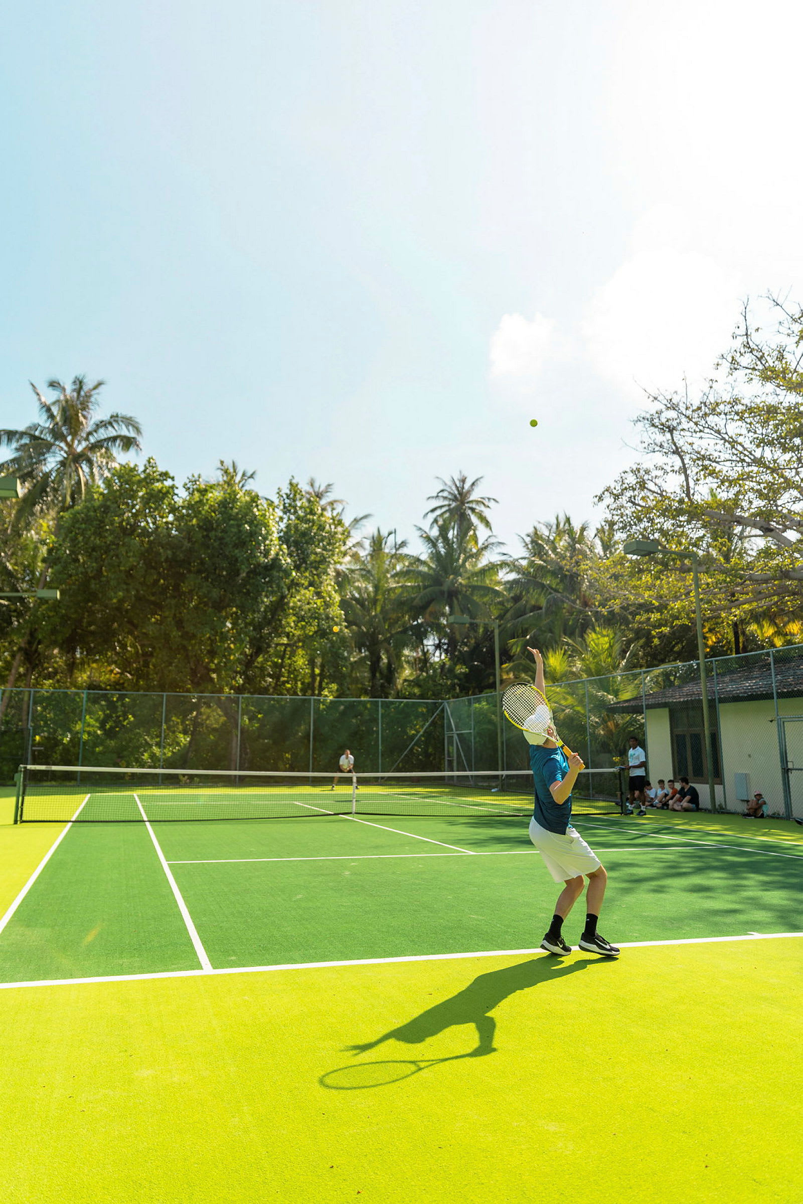 En person spelar tennis på en utomhusbana omgivet av träd. (AI-genererad text)
