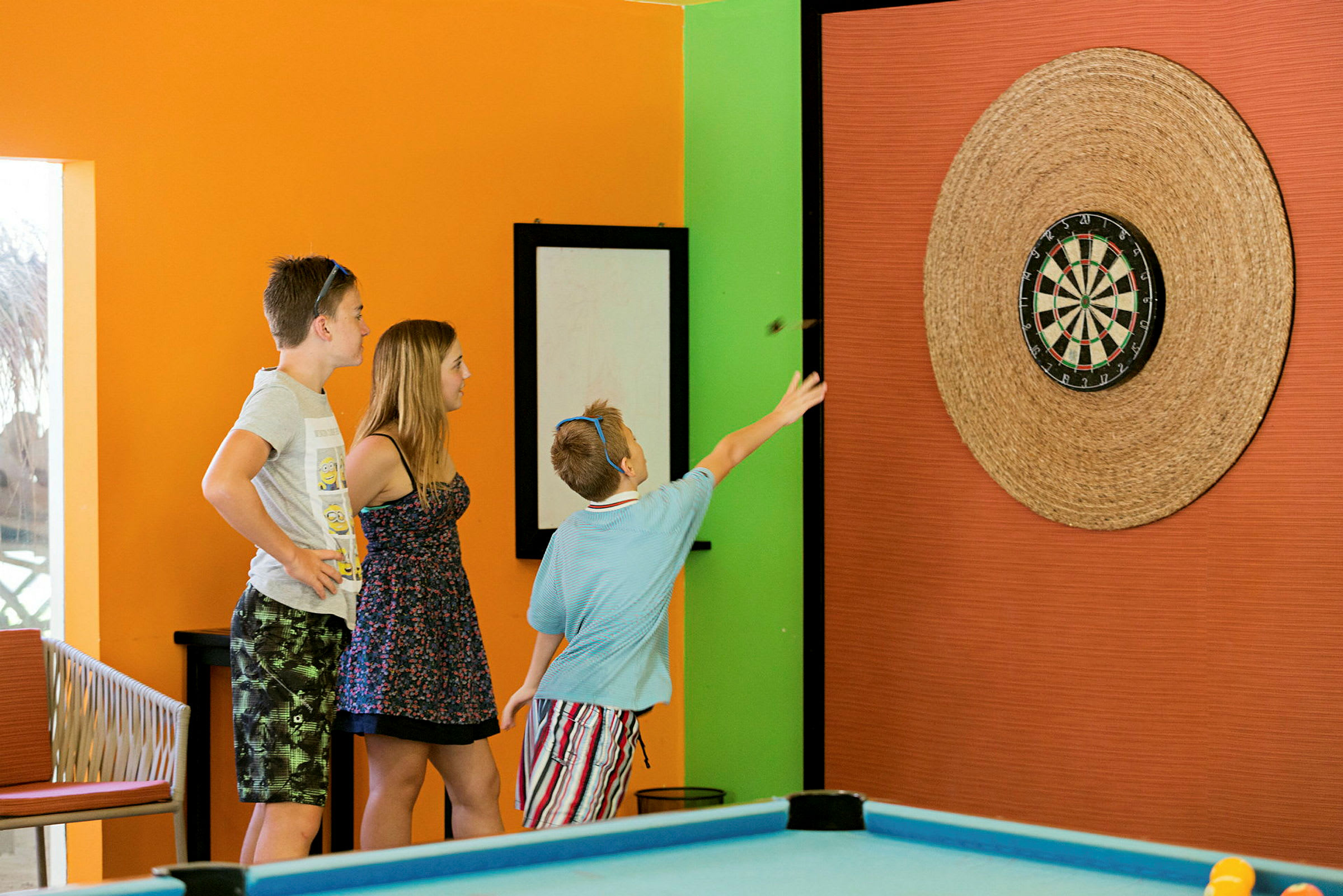 Tre personer spelar dart i ett färgglatt rum. (AI-genererad text)