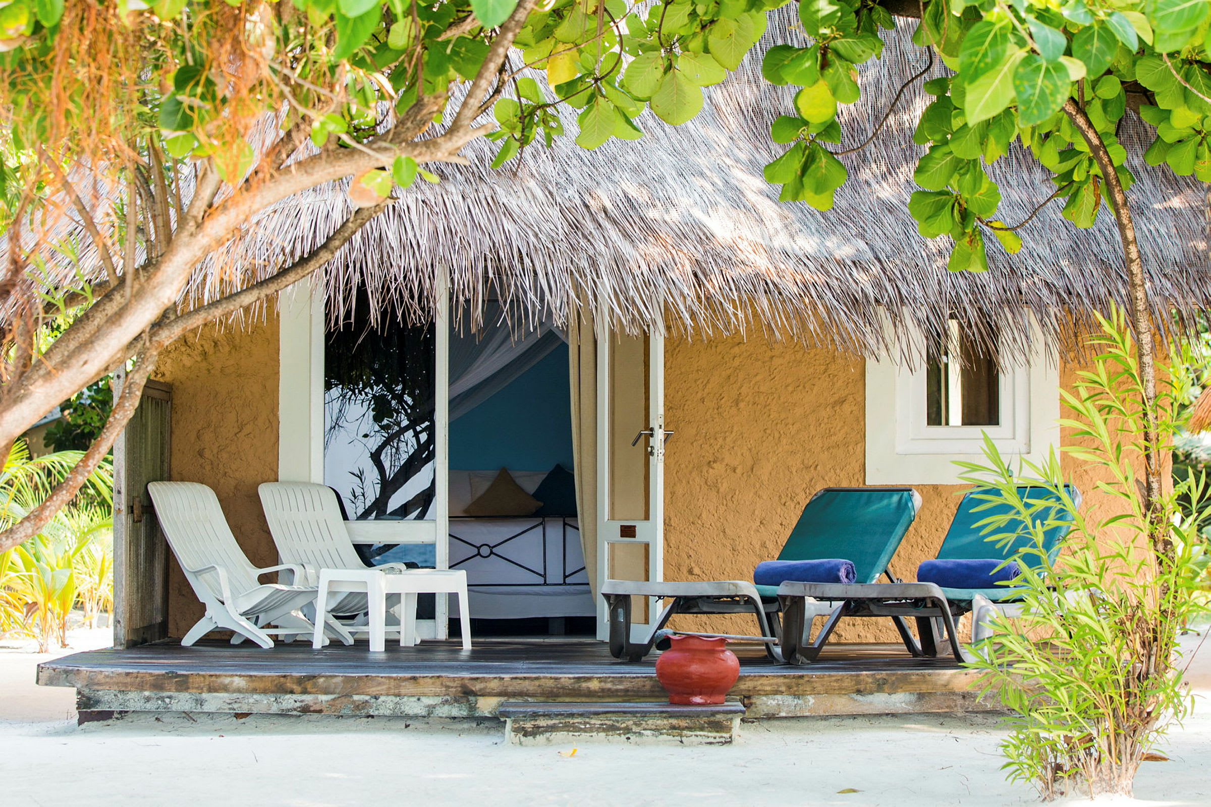 Strandbungalow med halmtak, sittgrupp och solstolar på terrass. (AI-genererad text)