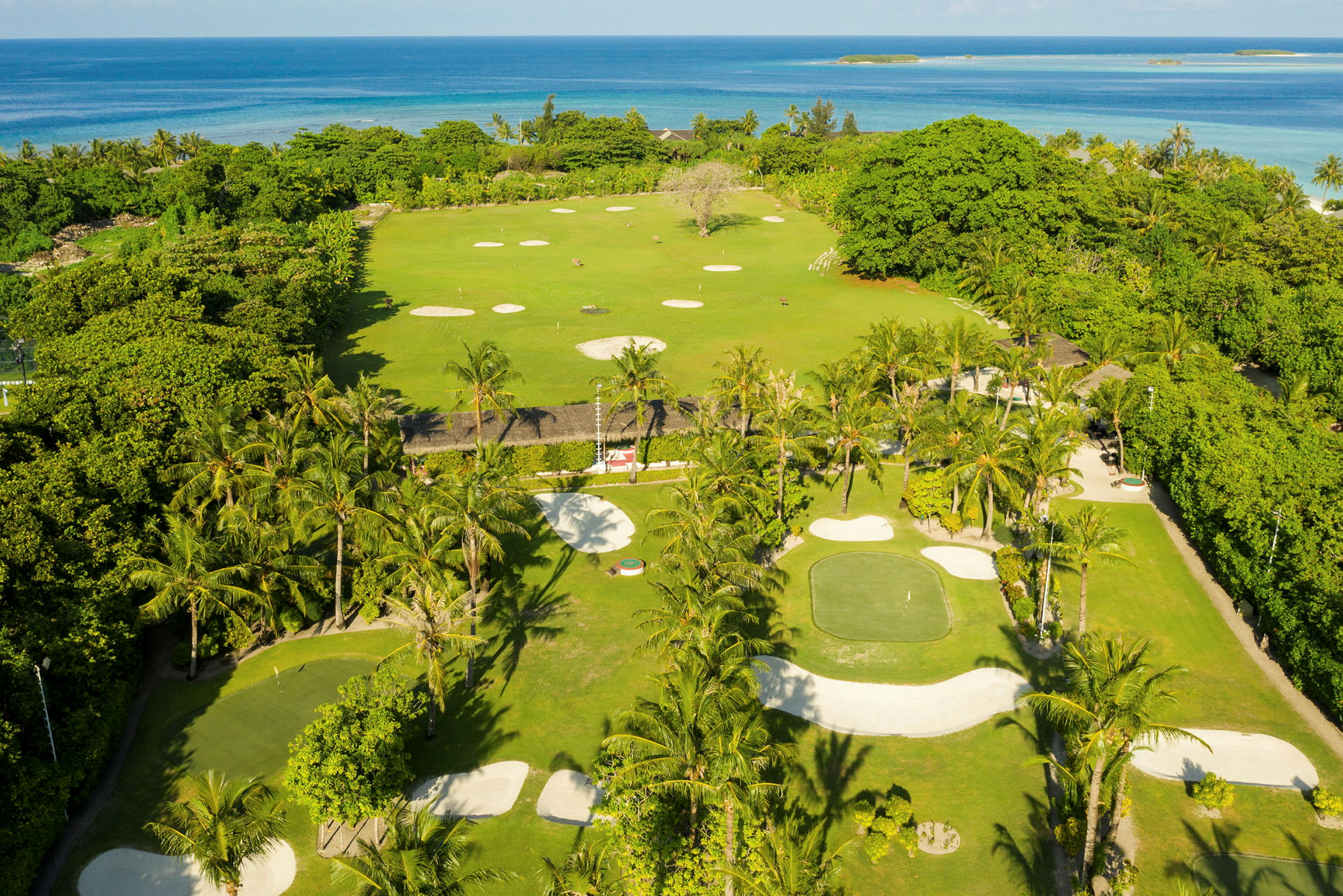 Utsikt över en golfbana med gröna ytor, sandbunkrar och palmer vid havet. (AI-genererad text)