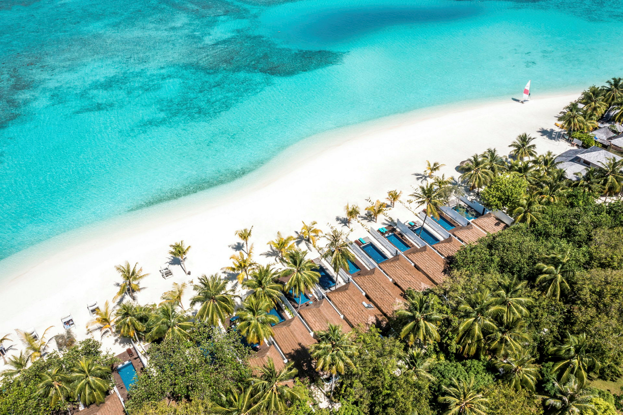 Flygfoto över en tropisk strand med vit sand, turkost hav, palmer och privata bungalower med pooler. (AI-genererad text)