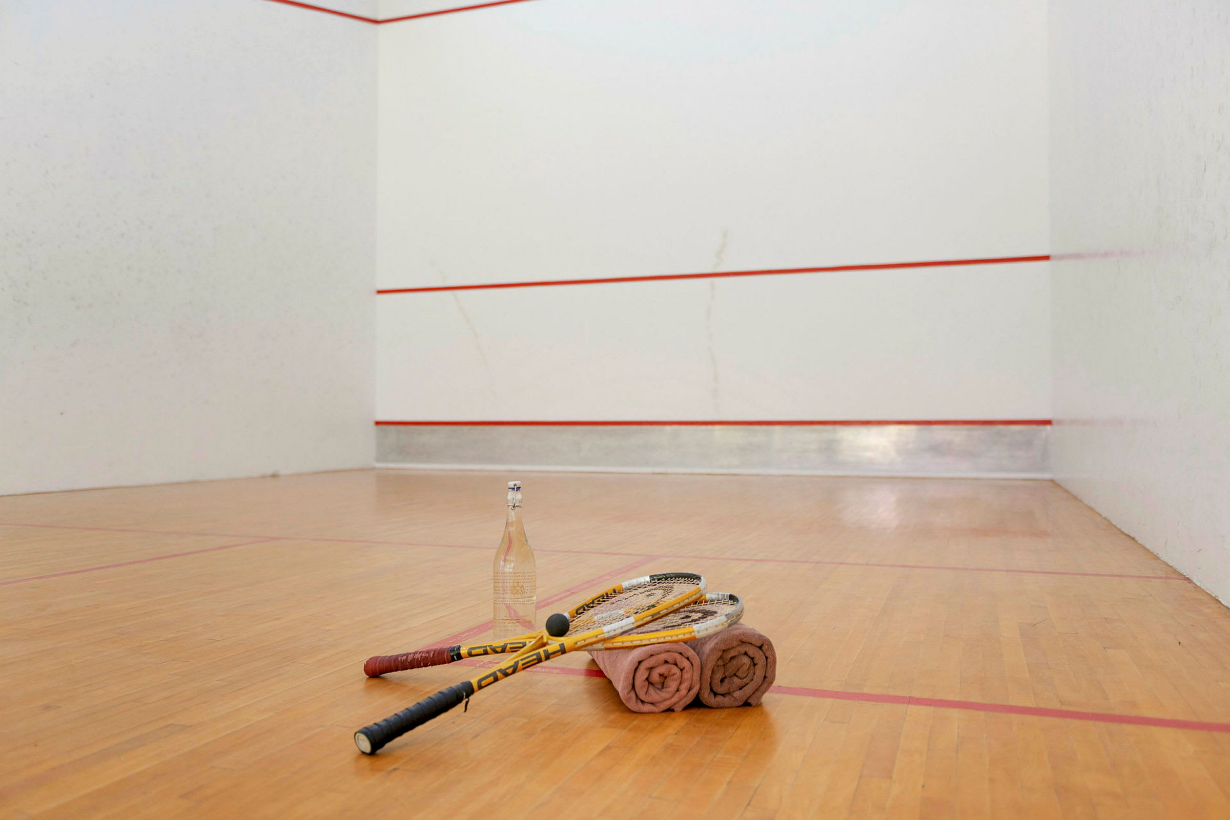 Squashrack, handdukar och en vattenflaska ligger på golvet på en squashbana. (AI-genererad text)