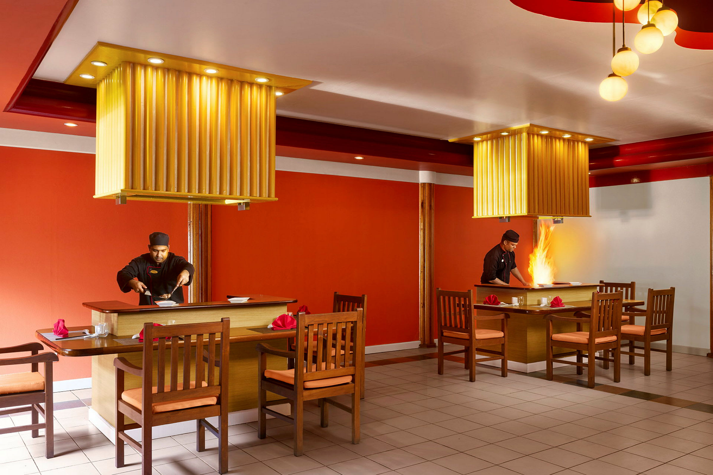 Två matbord med tillhörande stolar i en restaurang med orange inredning och taklampor. (AI-genererad text)
