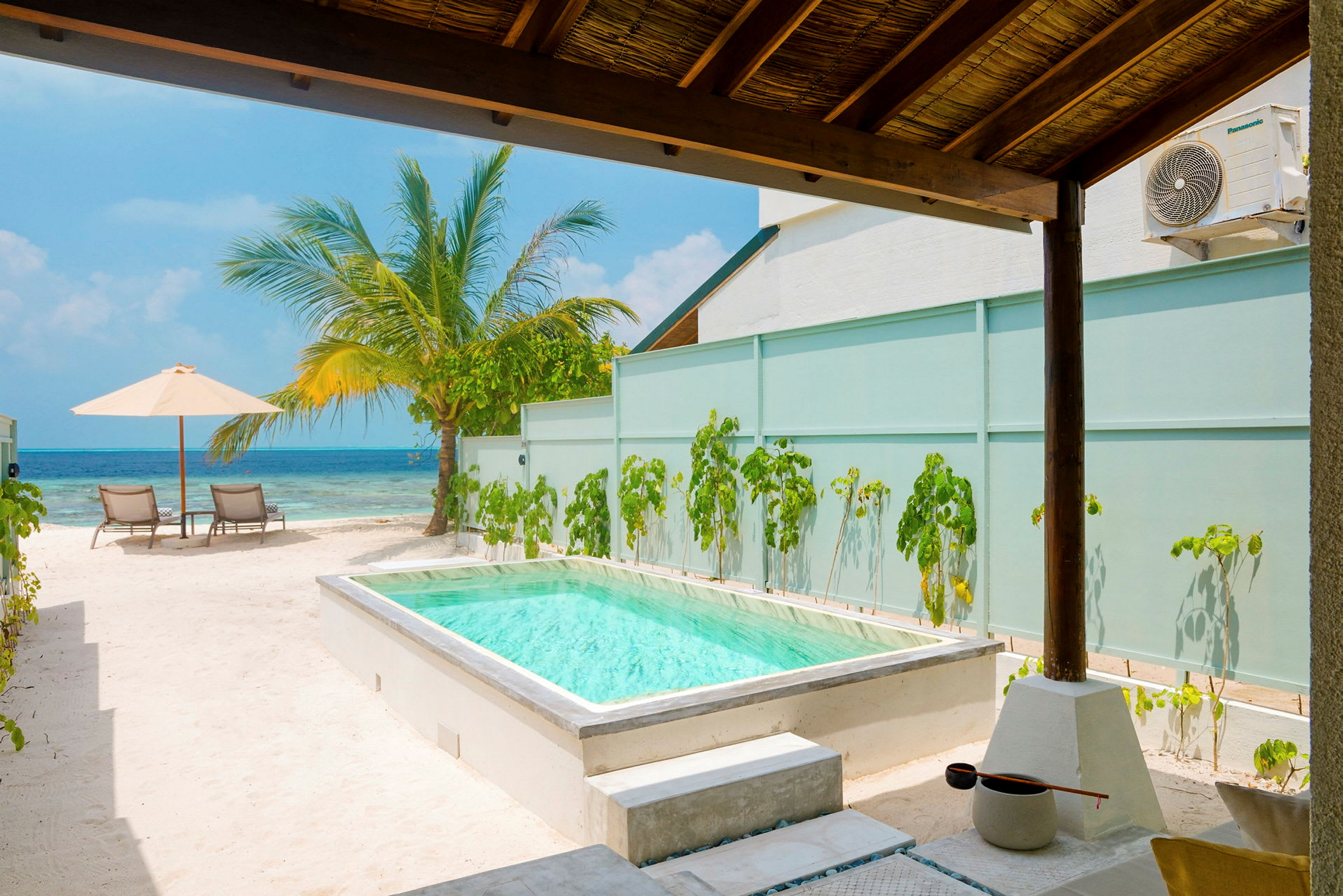 Private pool med utsikt mot havet, omgiven av sand och palmträdunder skuggande tak. (AI-genererad text)