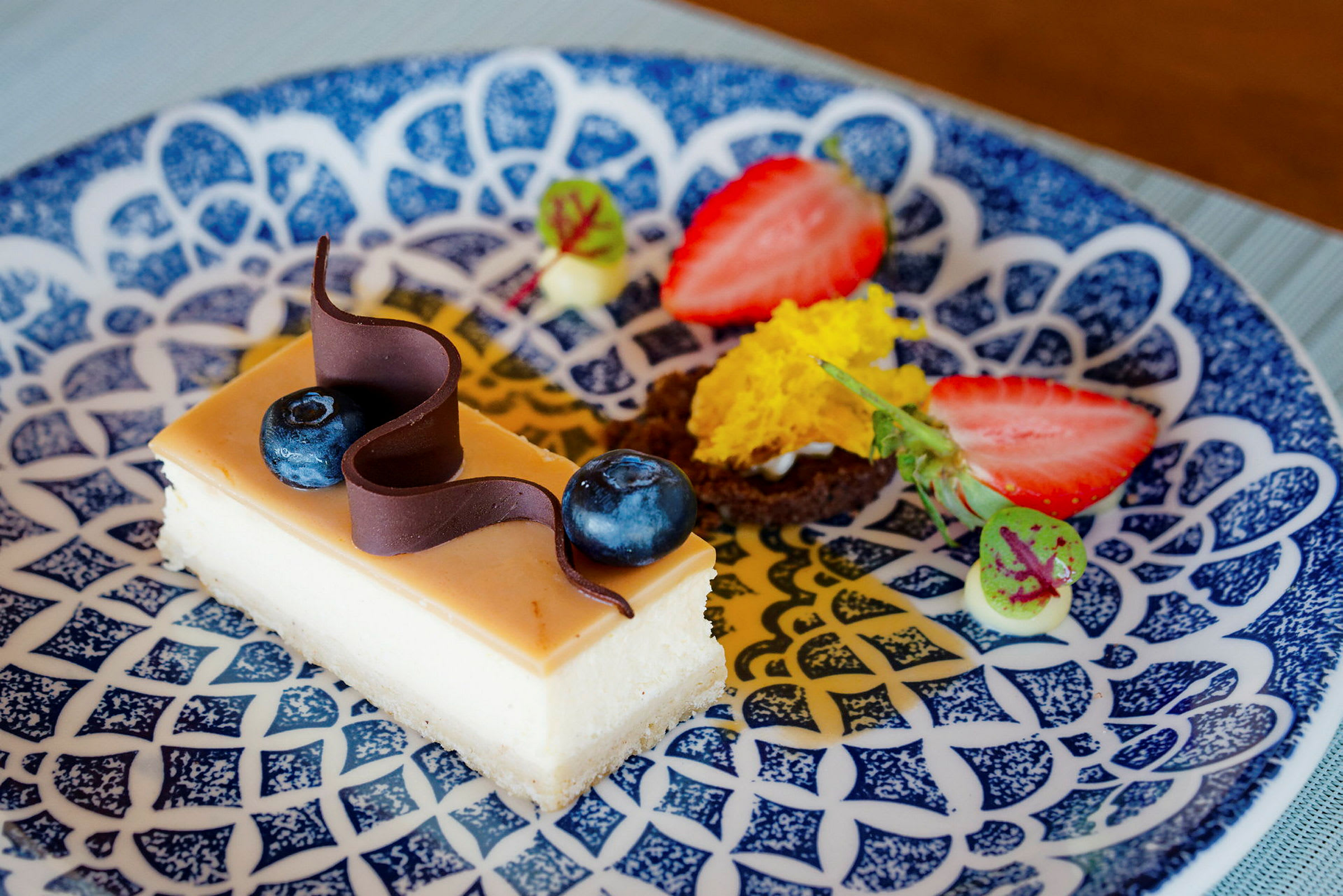 En dessert med en bit kaka dekorerad med blåbär och choklad på en mönstrad tallrik. (AI-genererad text)