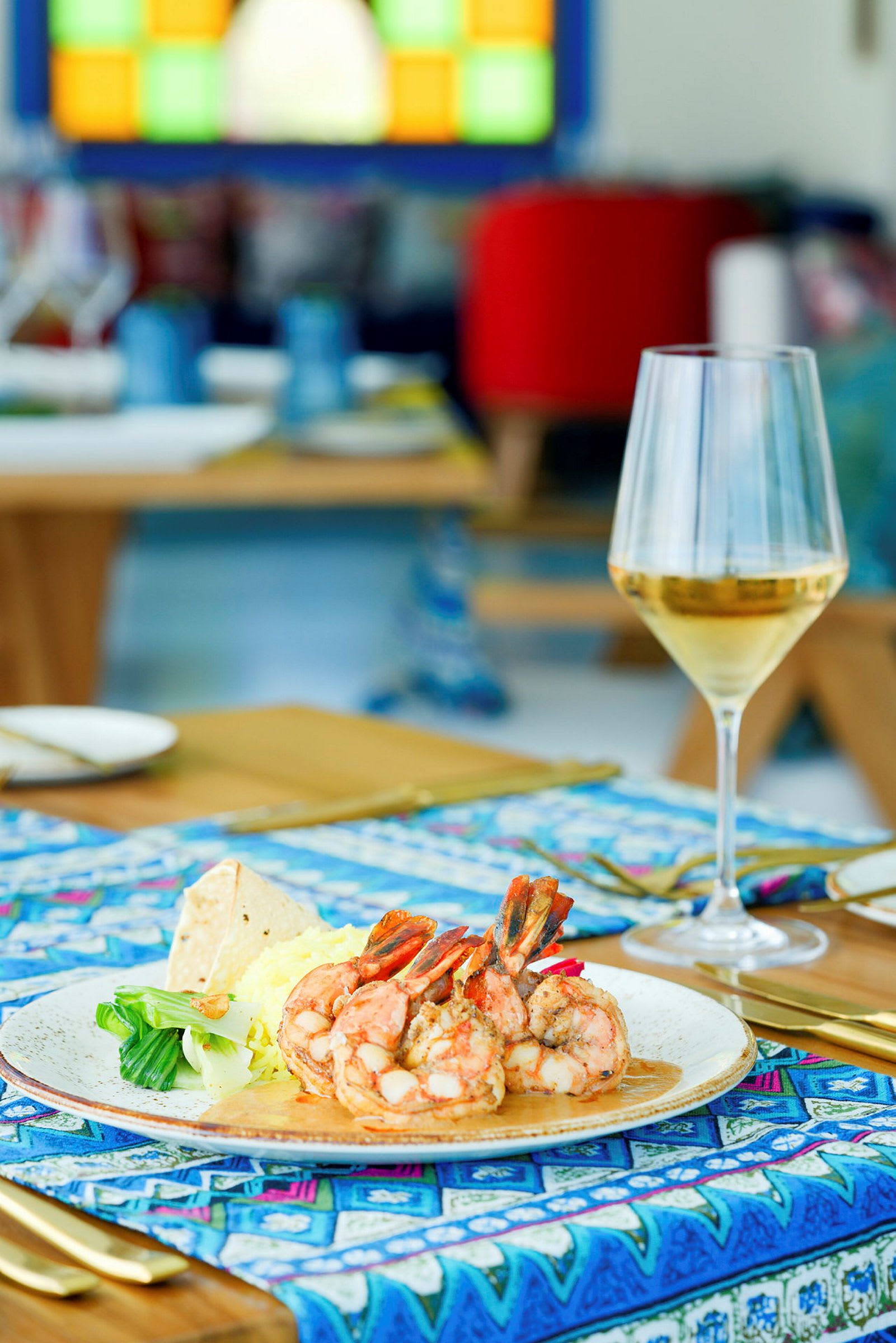 En tallrik med räkor, grönsaker och ris samt ett glas vin på ett dukat bord. (AI-genererad text)