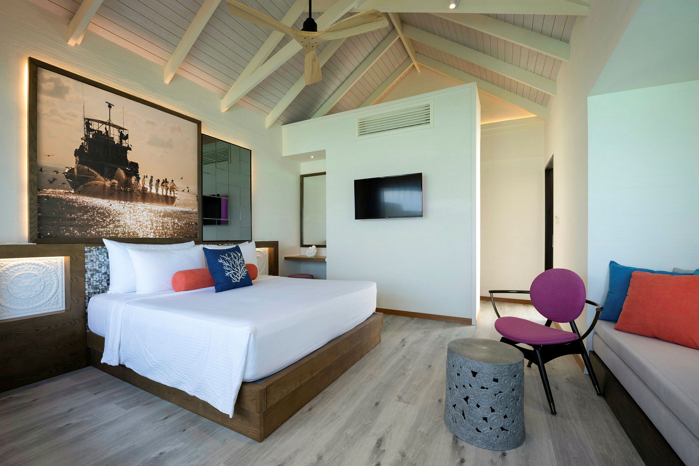 En modern hotellrum med en stor säng, färgstarka kuddar och ett väggmonterat tv. (AI-genererad text)