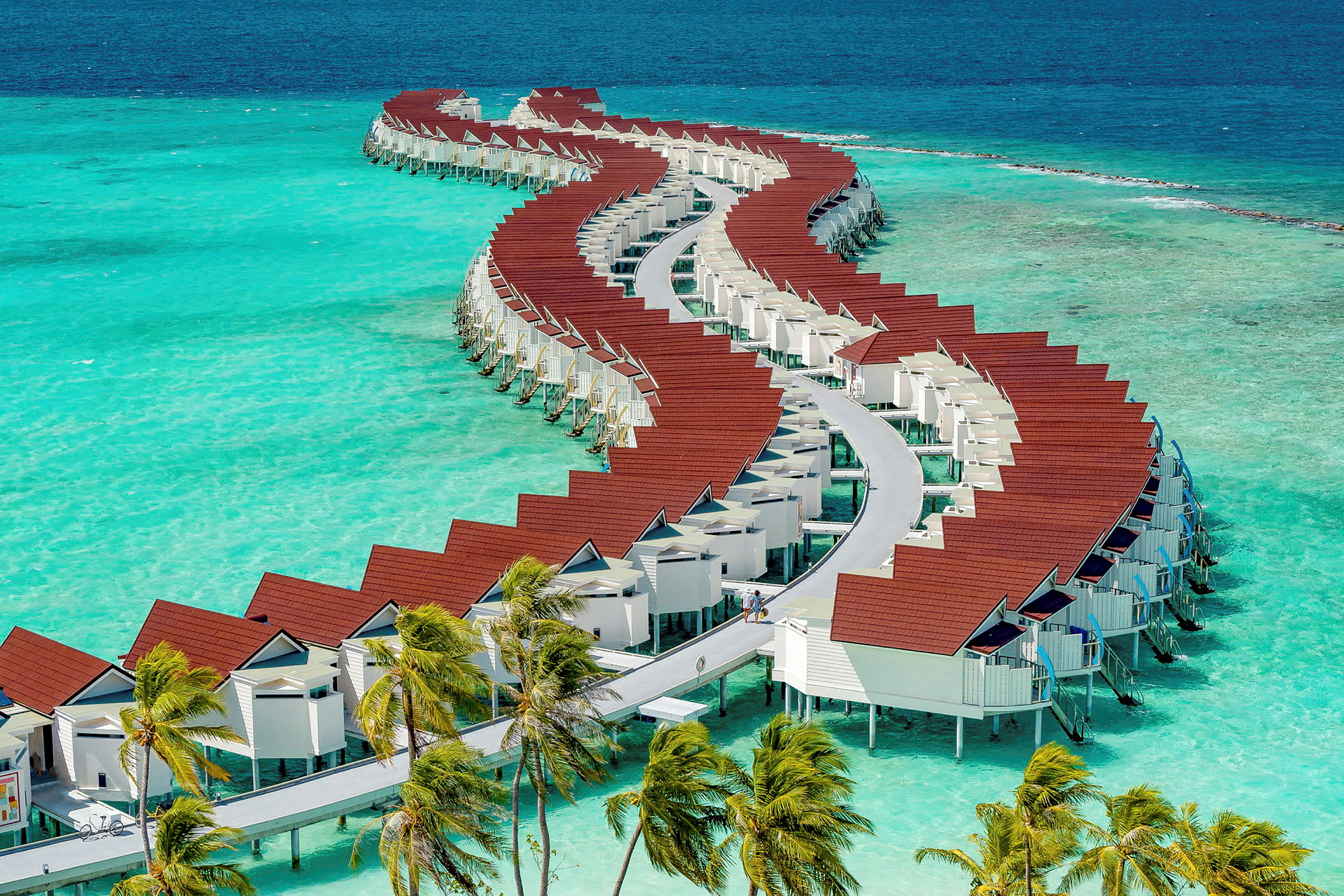 En rad av stilfulla övervattensbungalows med röda tak på azurblått vatten. (AI-genererad text)