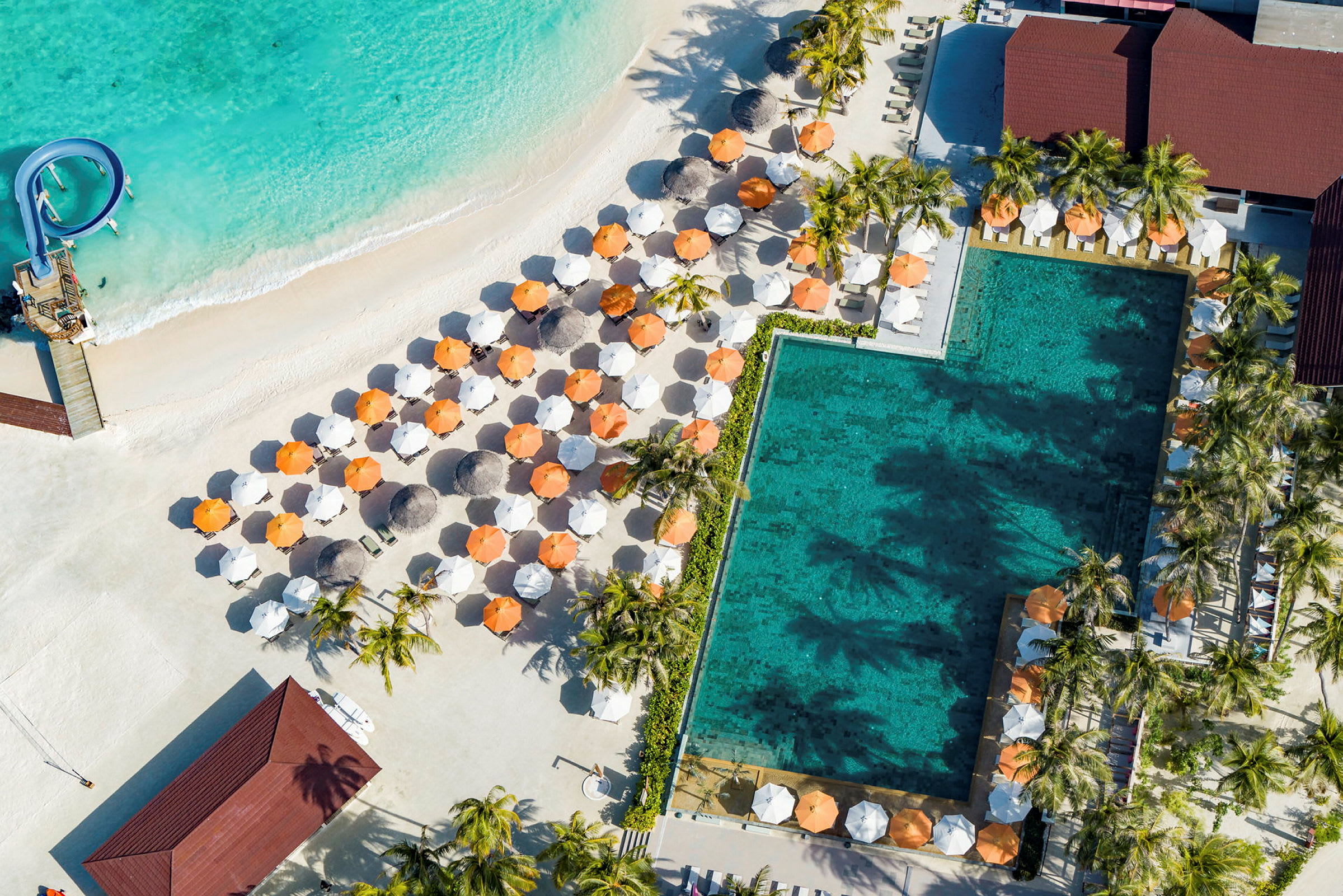Flygfoto av pool och sandstrand med parasoller och solstolar. (AI-genererad text)