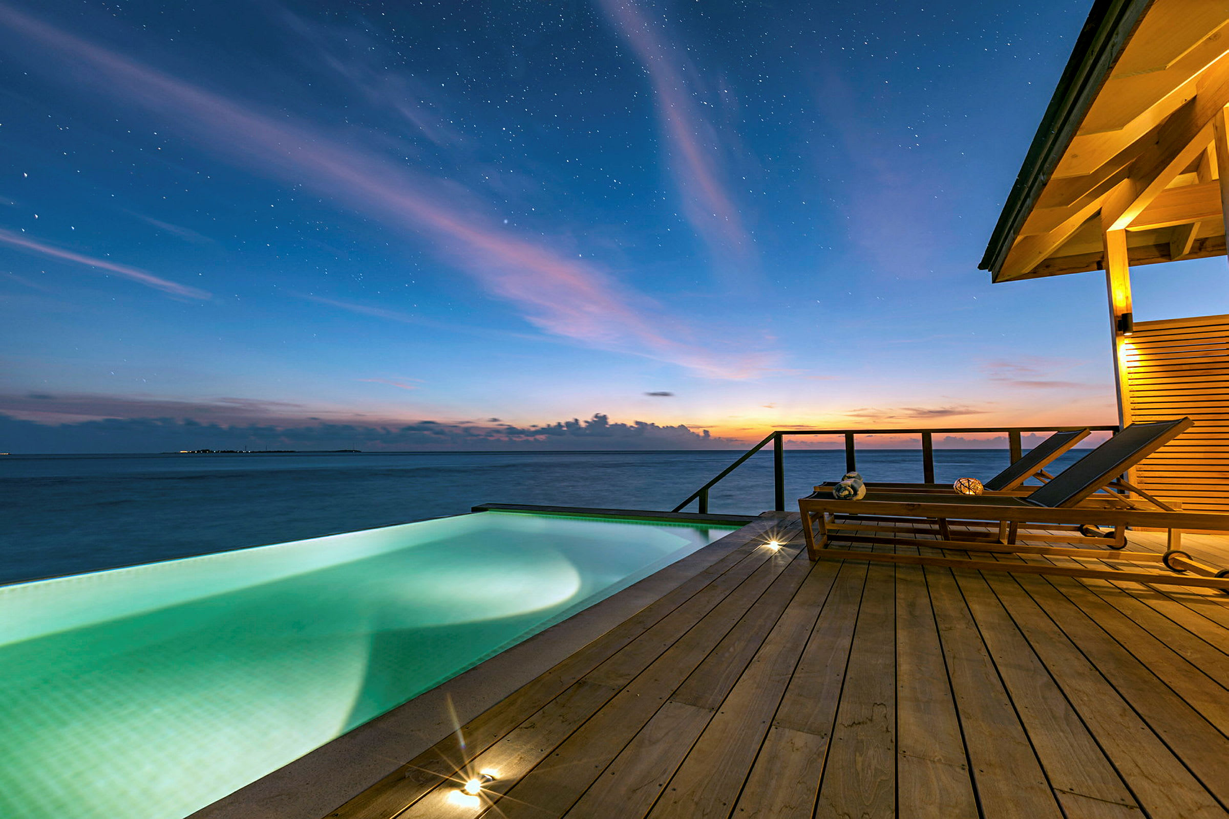 Bild föreställer en infinitypool vid en terrass med utsikt över havet under en stjärnklar kväll. (AI-genererad text)