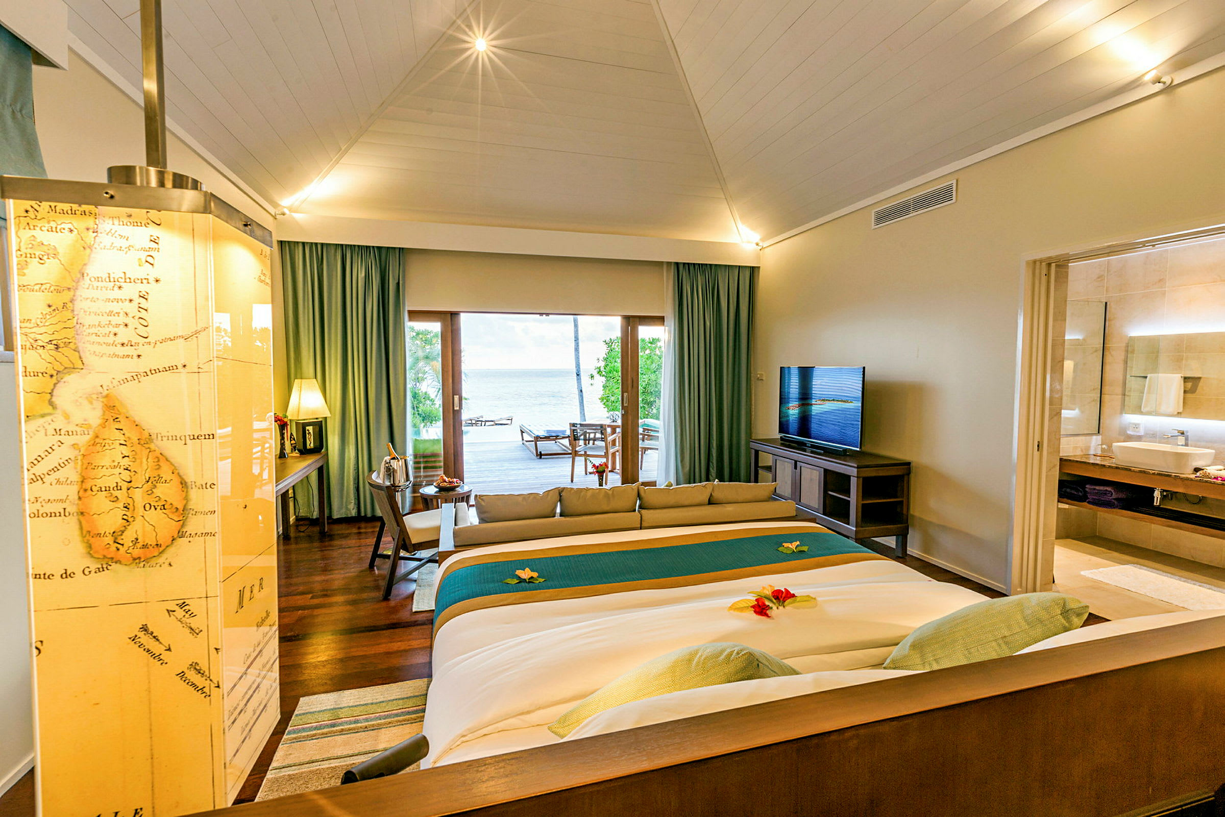 Ett hotellrum med en stor säng, TV, sittområde och utsikt över vattnet. (AI-genererad text)