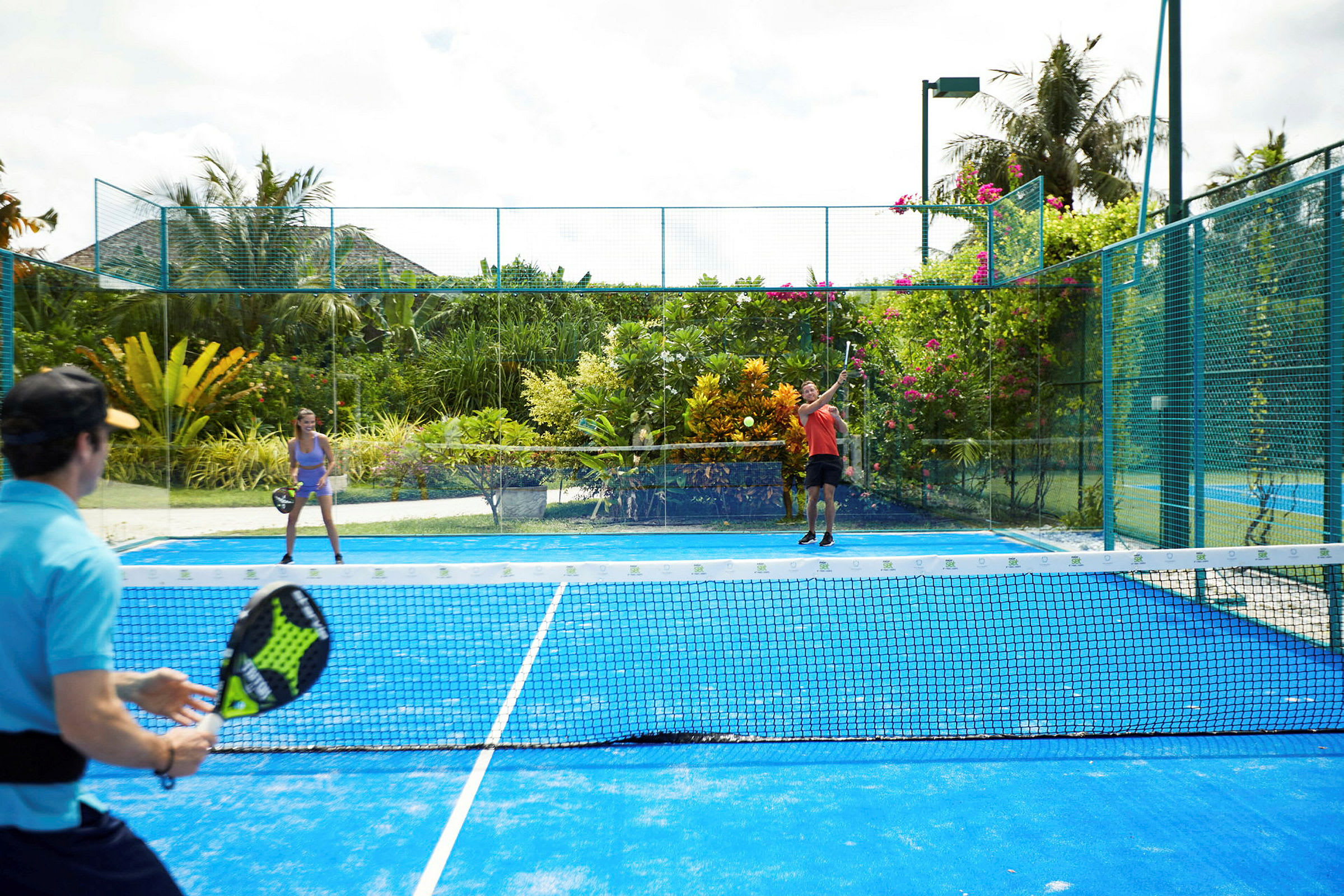 Personer spelar padeltennis på en utomhusbana omgiven av frodig grönska. (AI-genererad text)