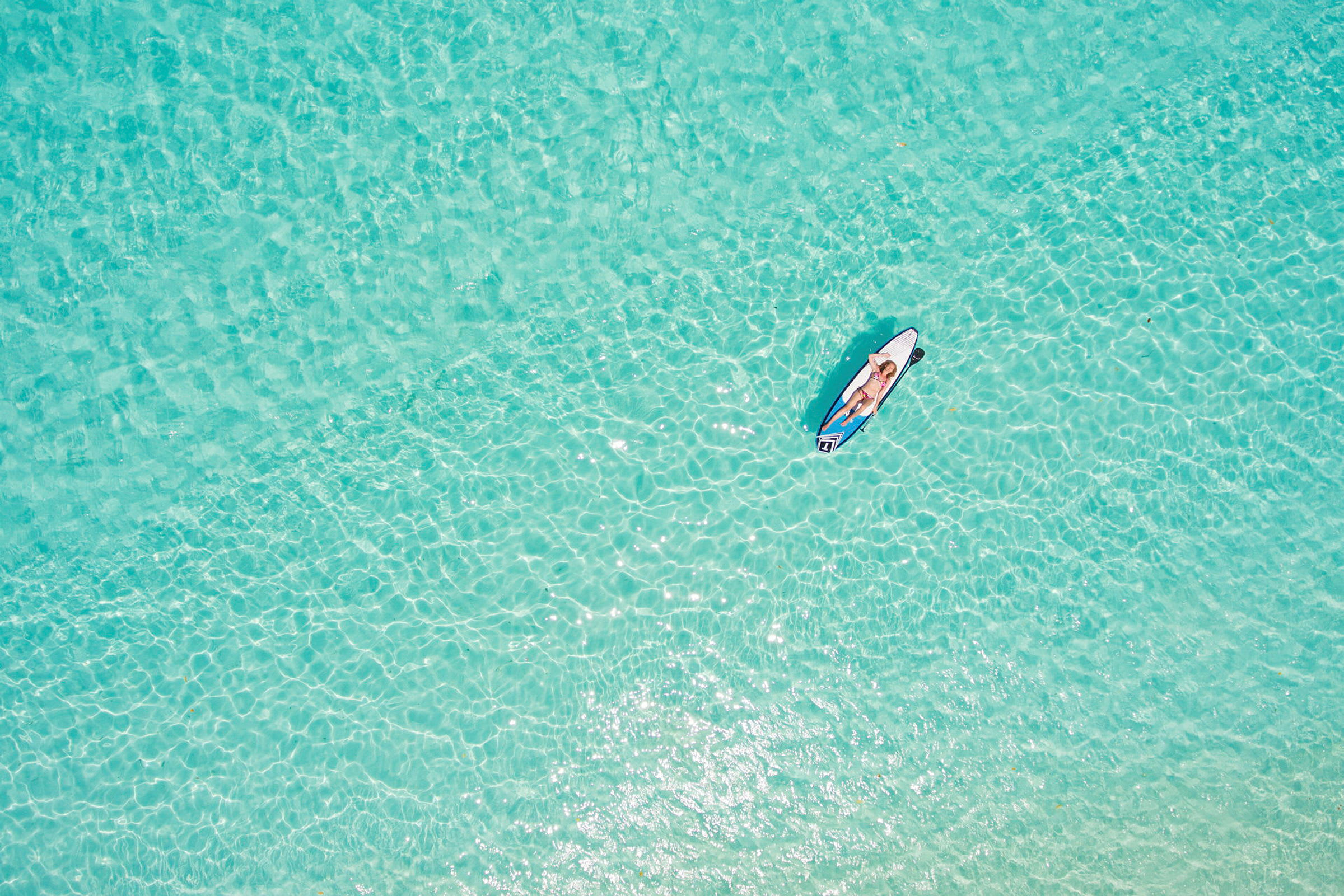 En person ligger på en paddleboard på klart turkost vatten. (AI-genererad text)