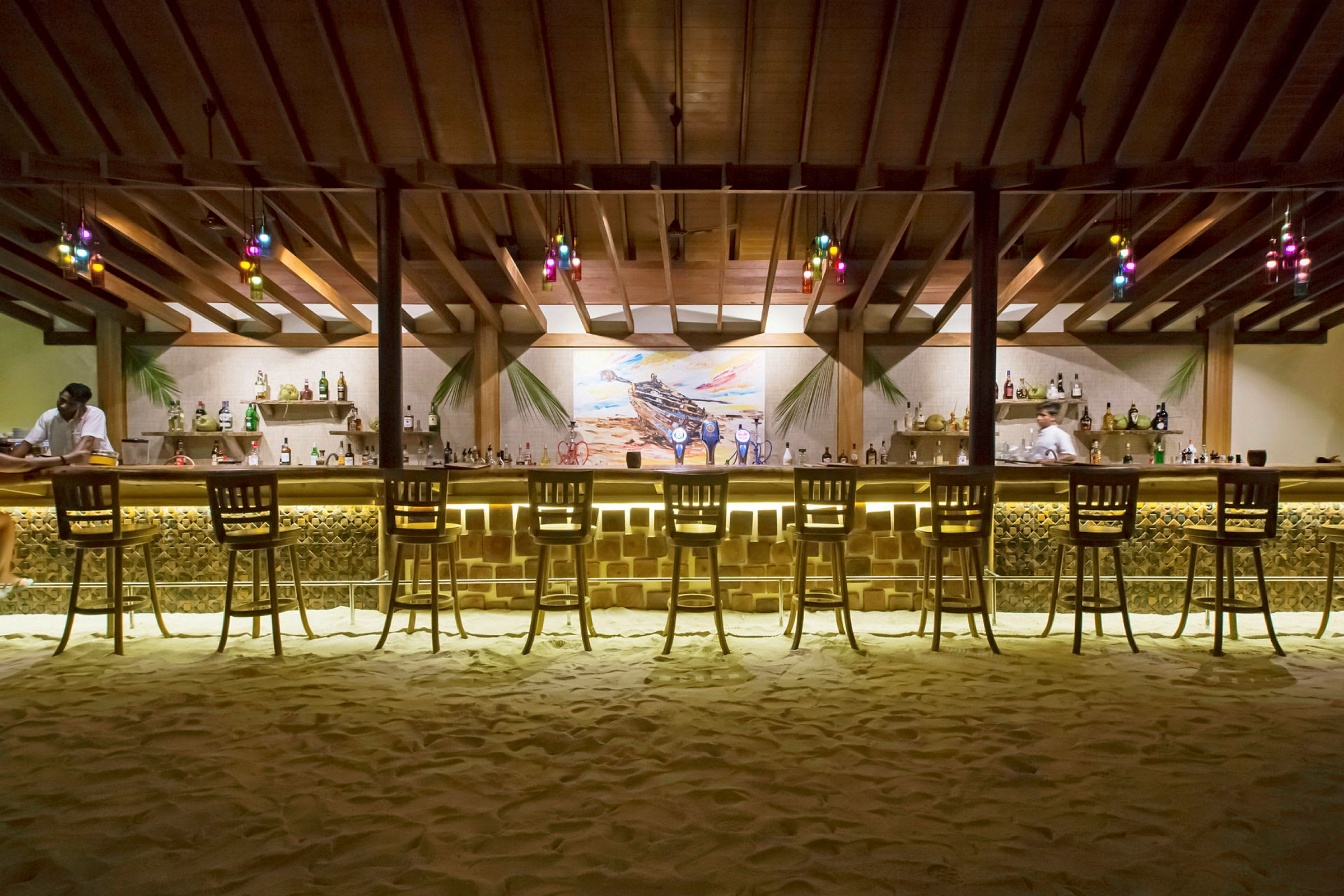 En strandbar med högt tak, upplyst bardisk och stolar framför. (AI-genererad text)