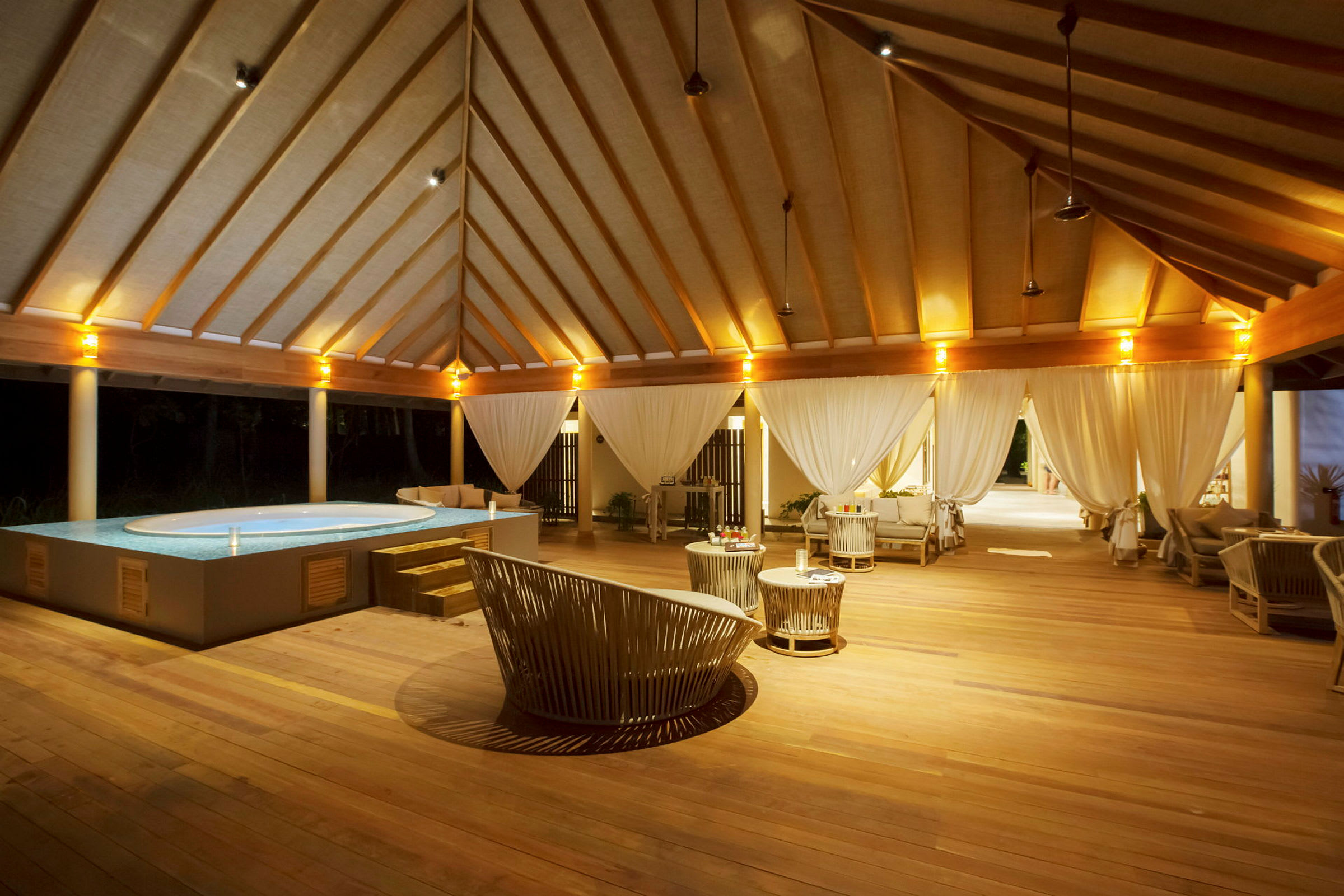 En lyxig utomhuslounge med pool och trämöbler, belyst på kvällen. (AI-genererad text)
