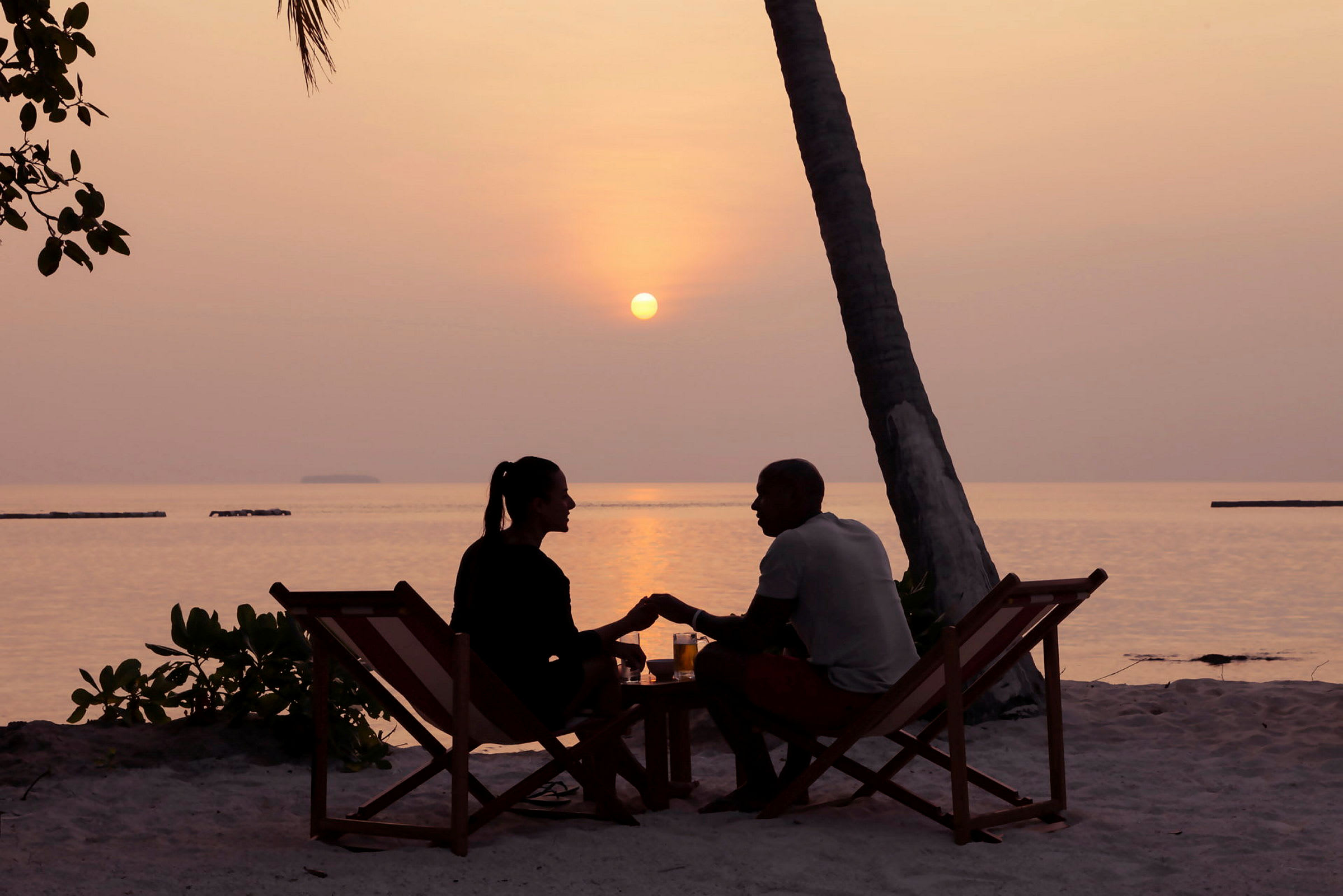 Ett par sitter på solstolar vid stranden under en solnedgång. (AI-genererad text)