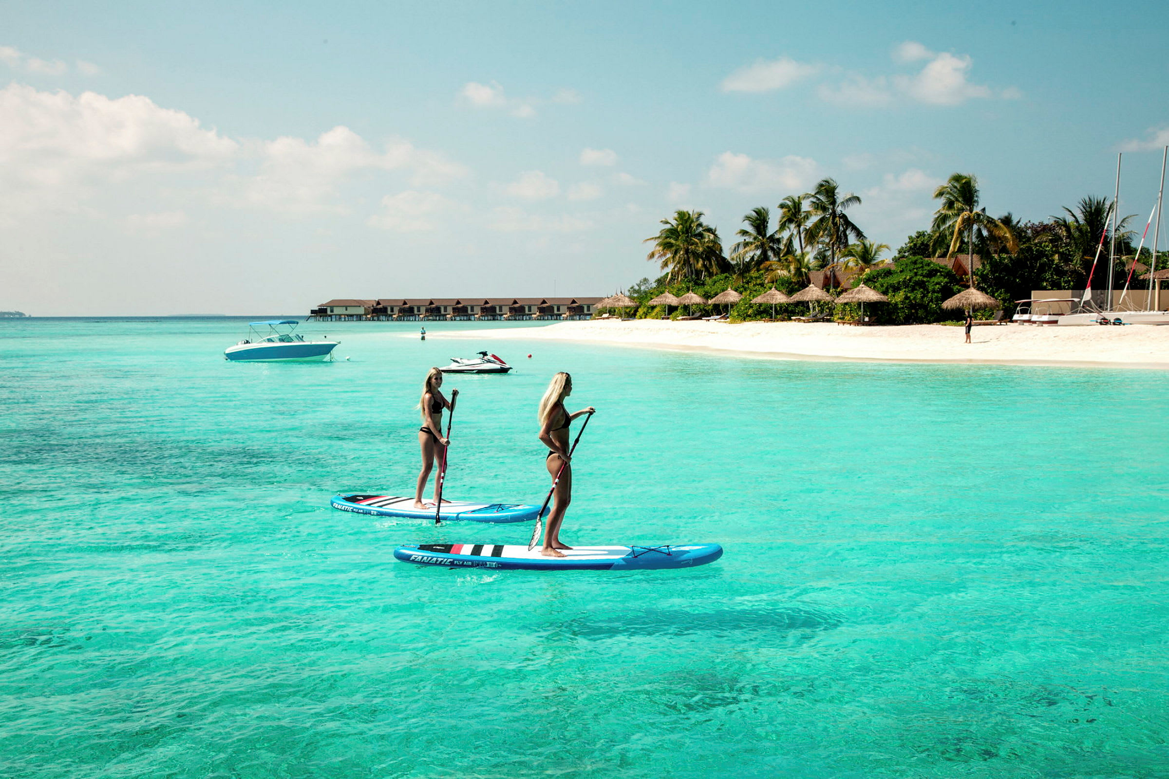 Två personer står på paddleboards i klart turkost vatten nära en sandstrand. (AI-genererad text)