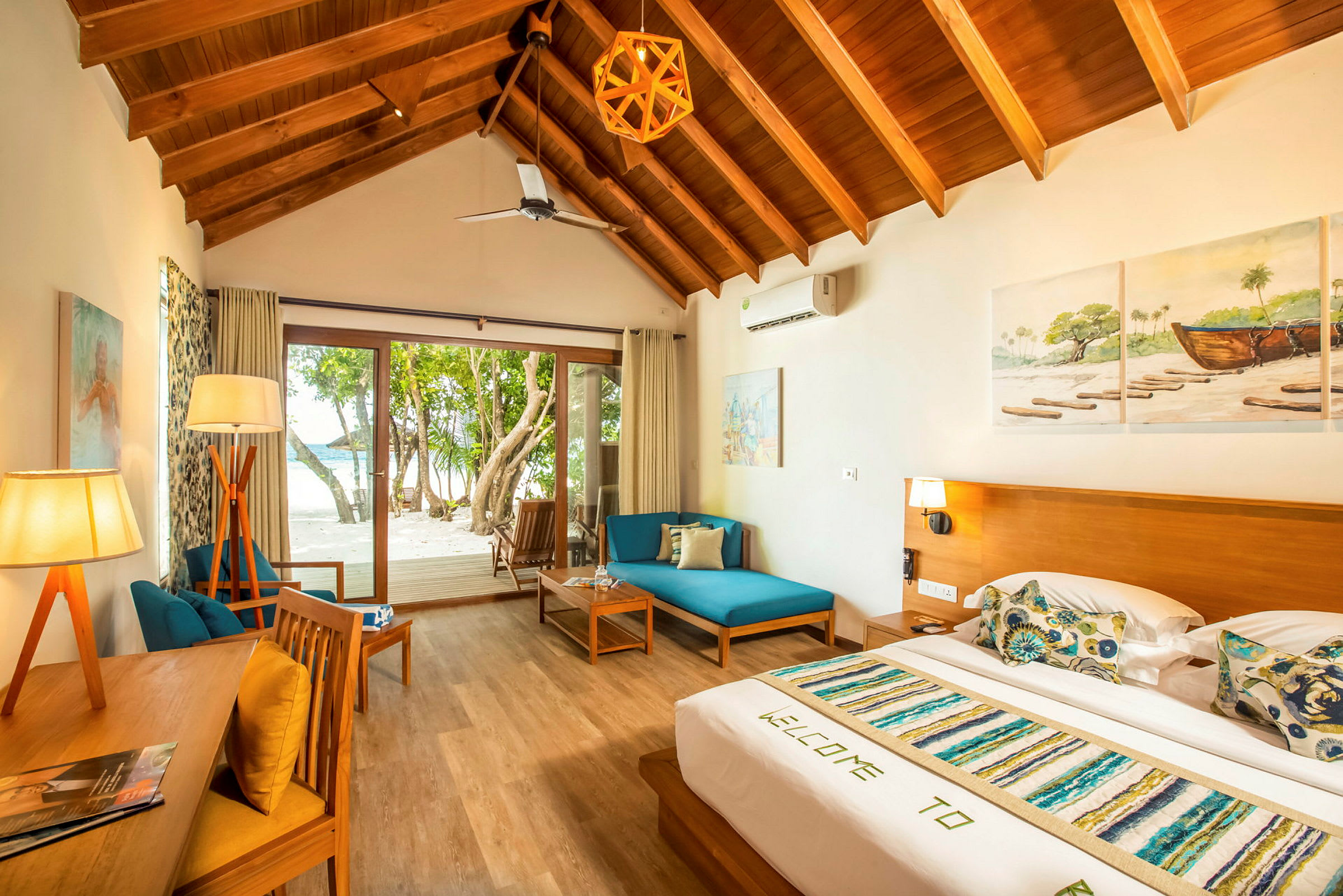 Ett semesterhotellrum med träinredning, säng, sittmöbler och glasdörrar som leder till en terrass och en strand. (AI-genererad text)