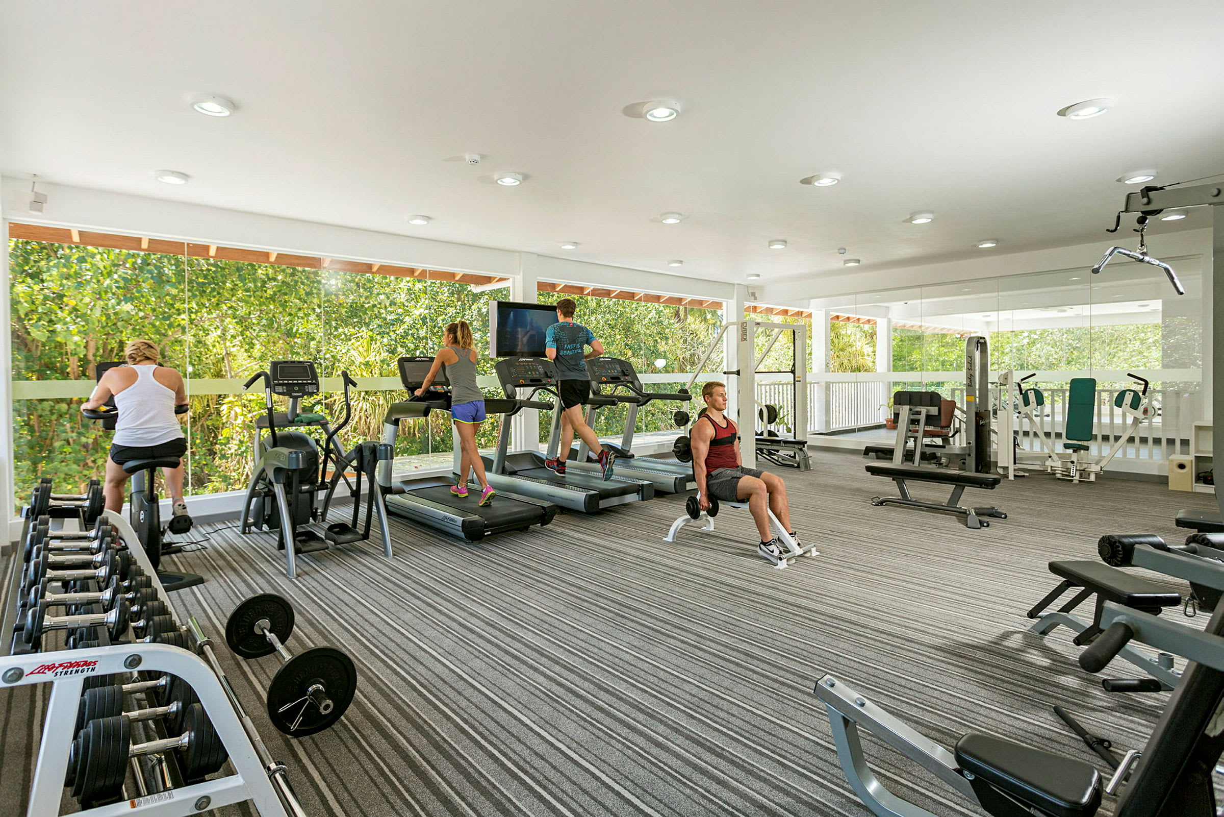 Ett gym med utrustning som löpband, cyklar och styrketräning, samt personer som tränar. (AI-genererad text)