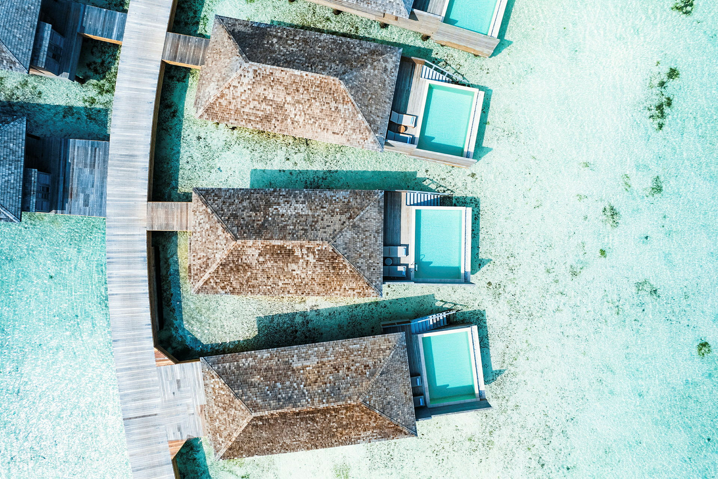 Flygfoto av strandvillor med privata pooler byggda över klart vatten anslutna med träbryggor. (AI-genererad text)