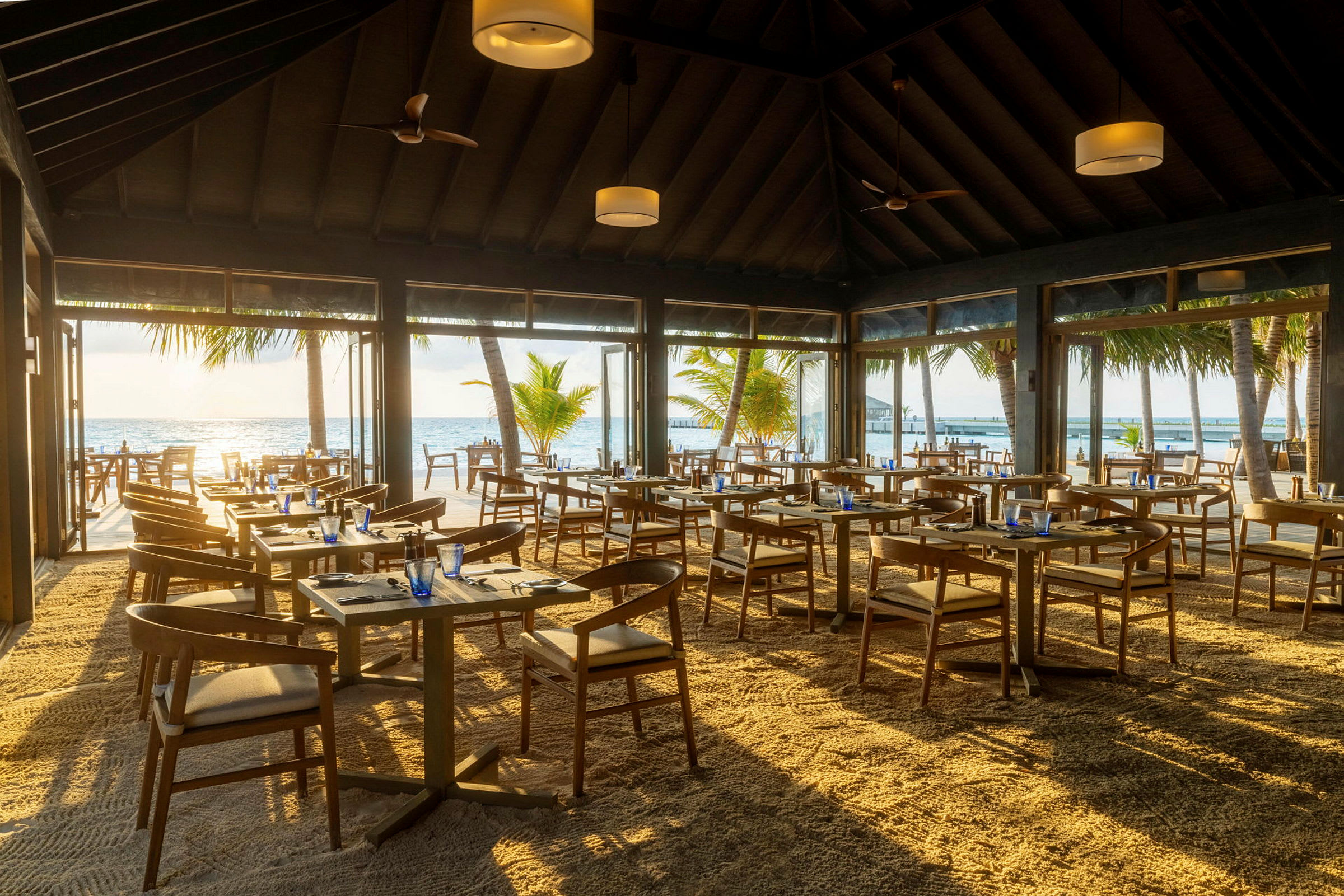Restaurang med sandgolv och utsikt över havet och palmträd. (AI-genererad text)