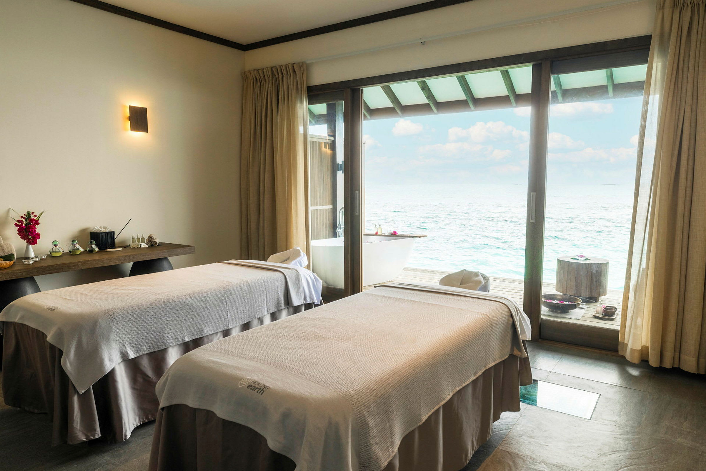 En spa-behandlingsrum med två massagebänkar och utsikt över havet. (AI-genererad text)