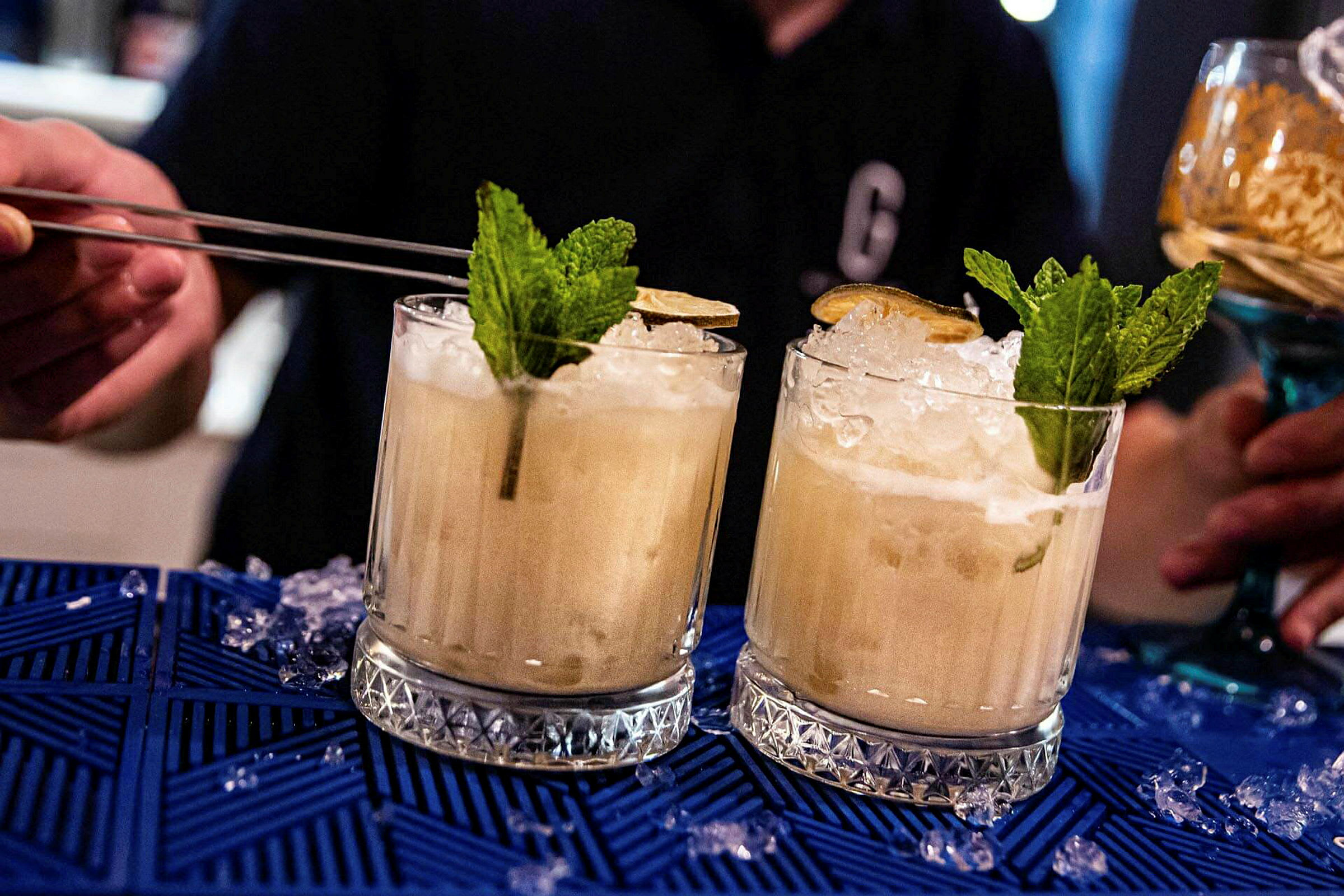 Två cocktails med is, mynta och lime på blå bordsduk. (AI-genererad text)